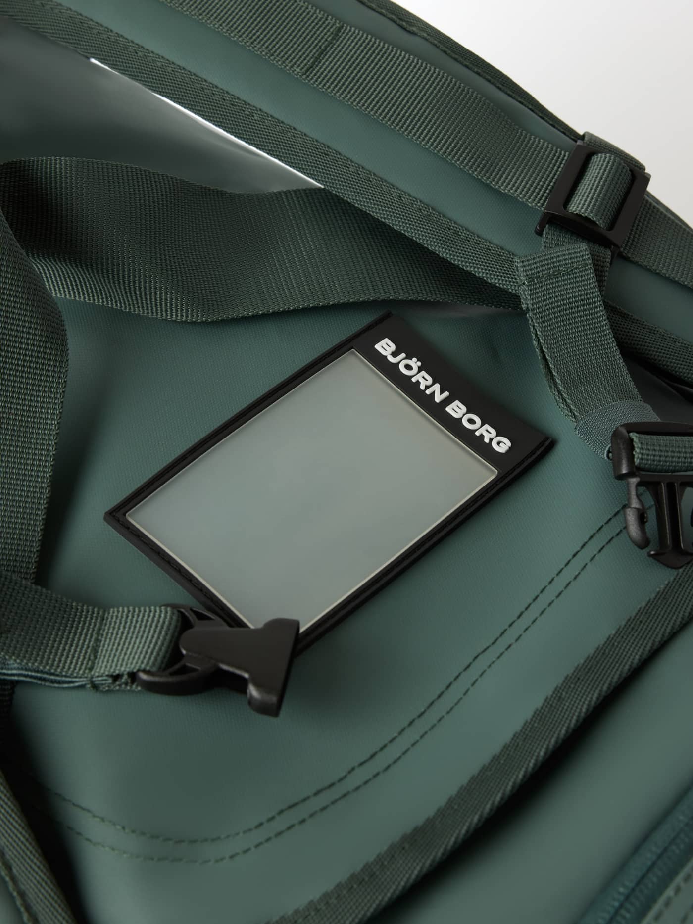 Detailed view of the Balsam Green (Green) Borg Duffle Bag 55L showing an address tag with a white logo and backpack straps. - Image 5