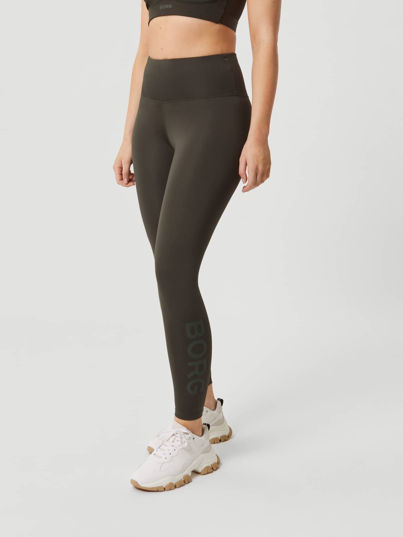 Front view of a model wearing the high-waist Björn Borg Borg Logo Tights in Peat (Green) for a stylish training fit. - Image 2