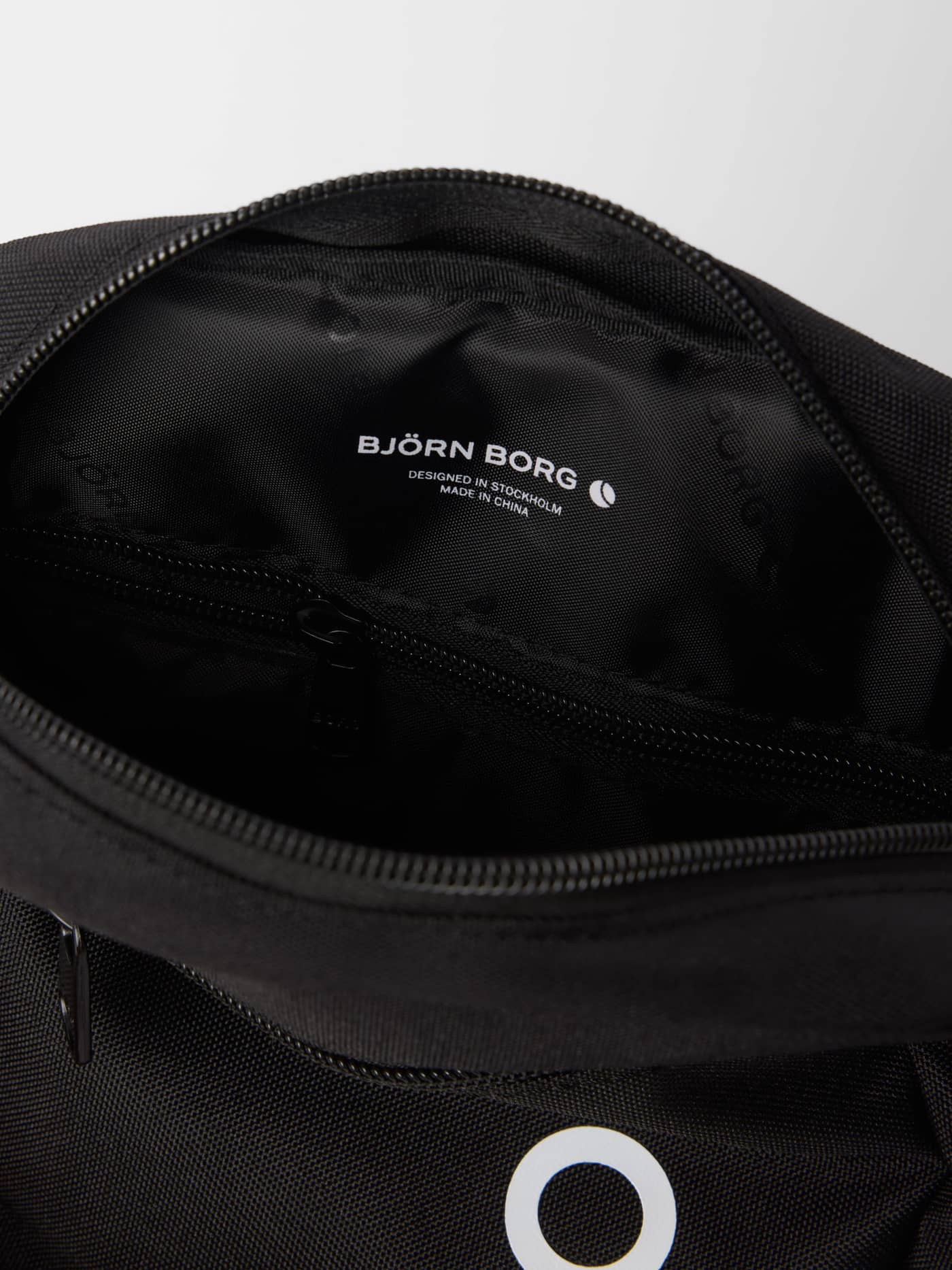 Detailed close-up of the black Core Crossover Bag 1,7L interior, featuring a zippered pocket and white brand logo. - Image 3