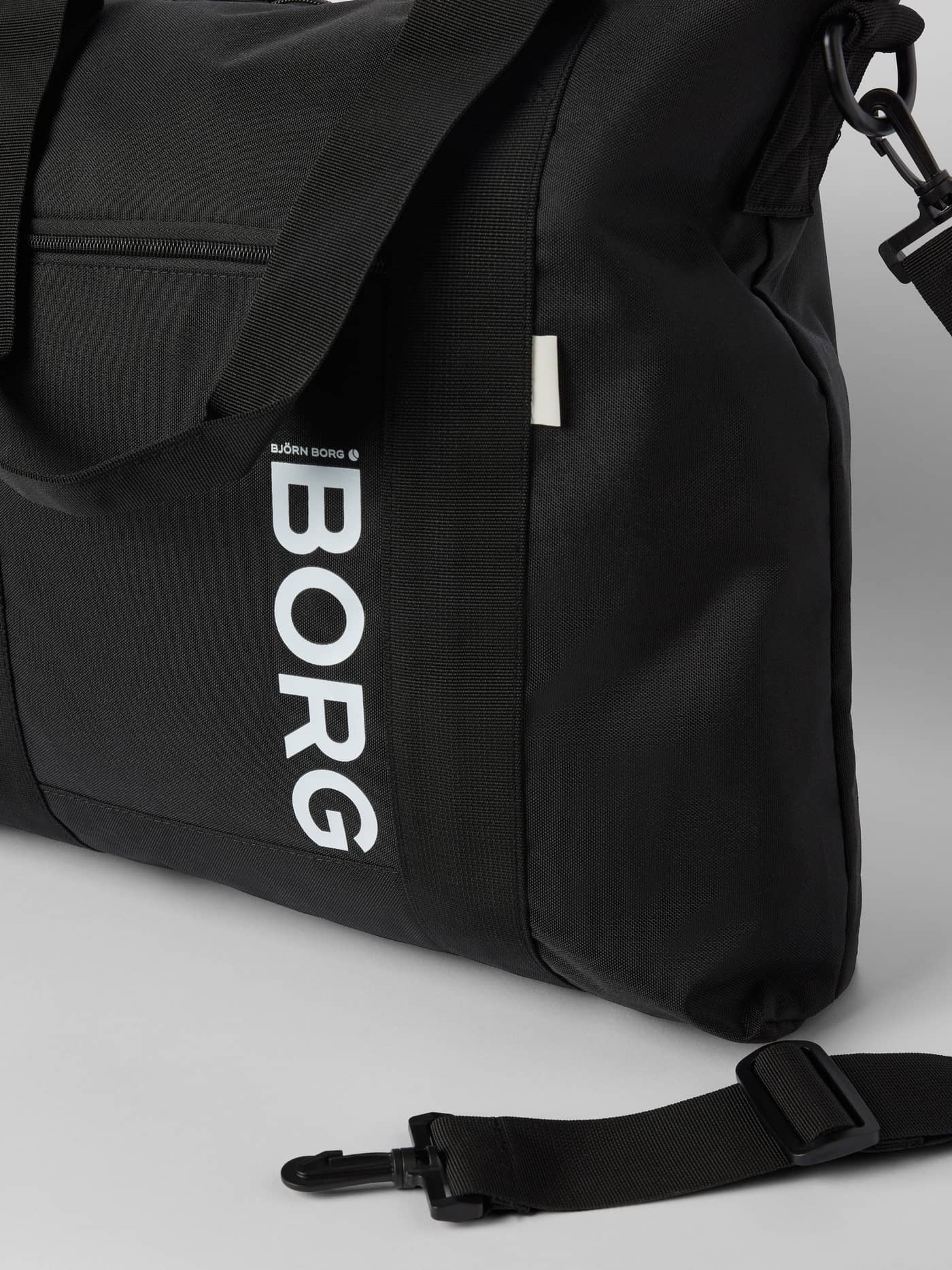 Close-up of the Core Tote Bag 23L in Black Beauty (Black) featuring a large white Borg logo and zippered front pocket. - Image 3