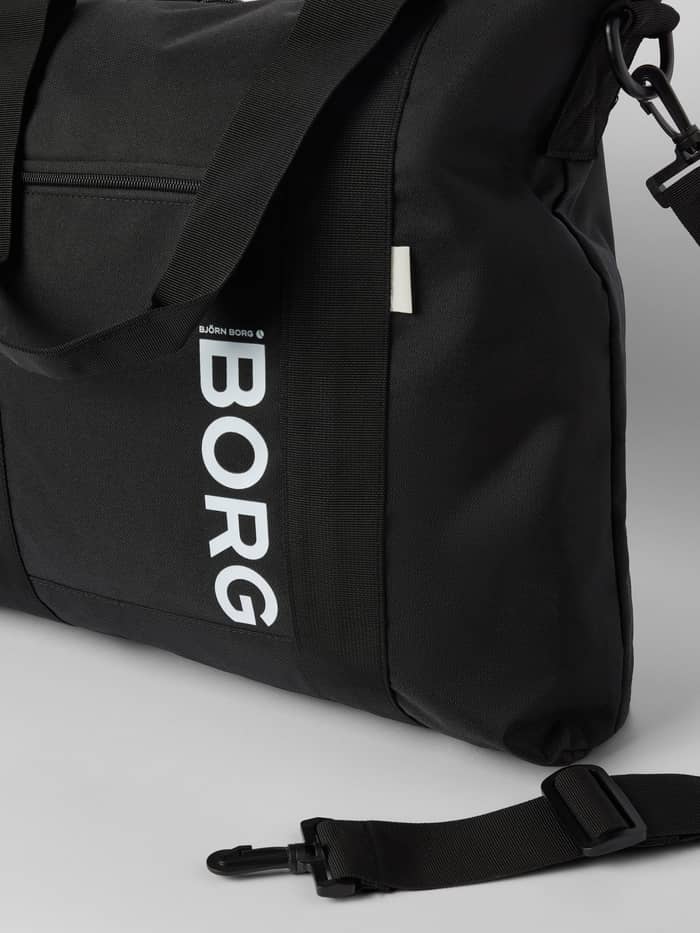 Close-up of the Core Tote Bag 23L in Black Beauty (Black) featuring a large white Borg logo and zippered front pocket. - Image 3