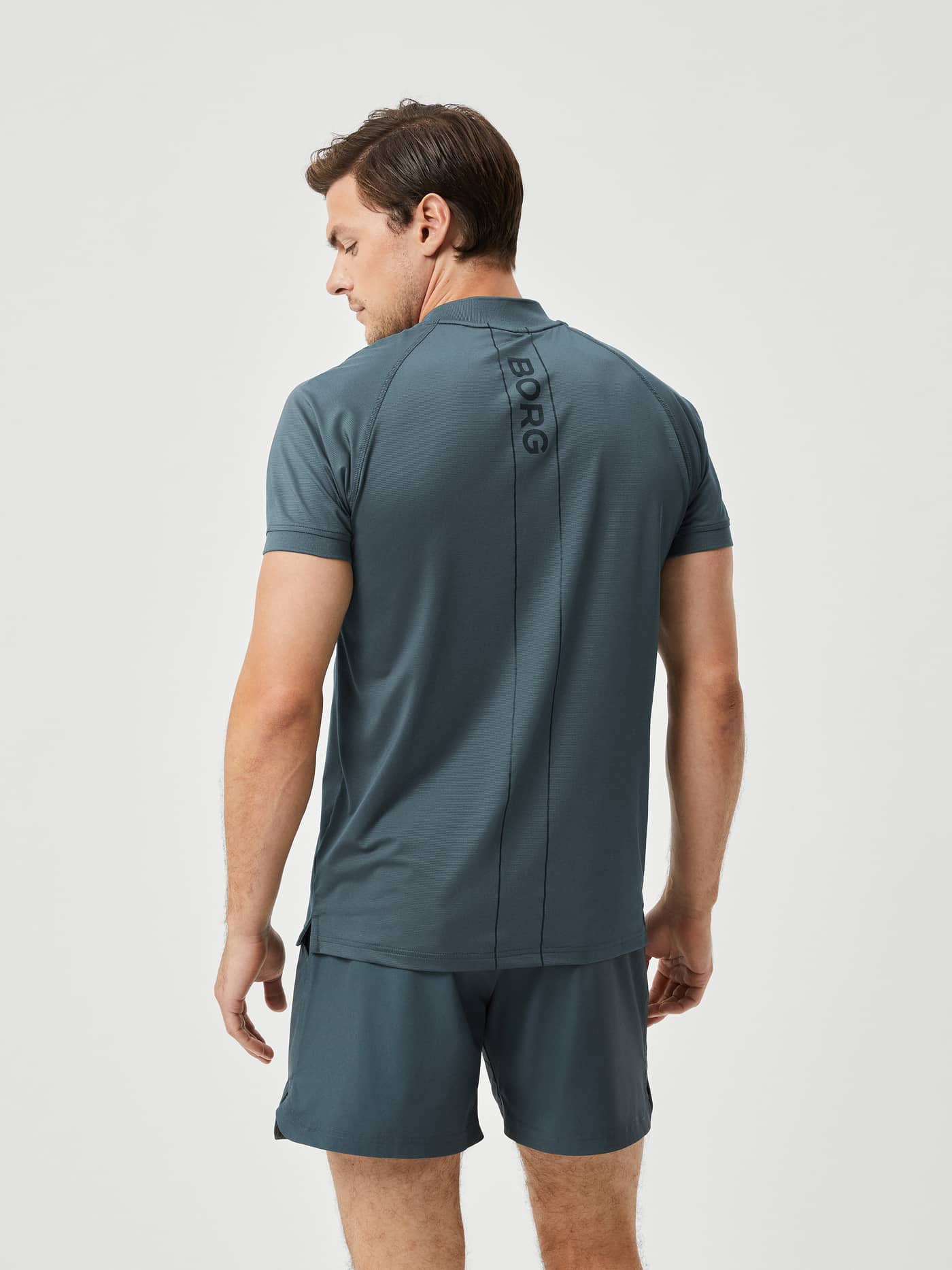 Back view of a man wearing the Ace Performance Zip Polo in Urban Chic (Green) with courtlines for tennis performance. - Image 2