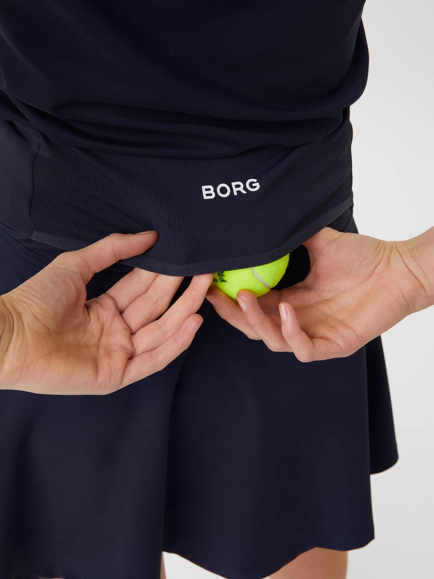 Close-up van de navy Ace Skirt Pocket met een achterzak voor tennisballen en een wit BORG-logo. - Image 4