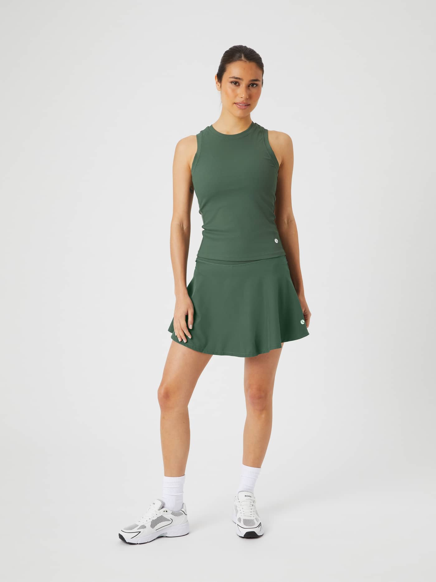 Full-body view of a model in the Björn Borg Ace Skirt Pocket in Cilantro (Green) with a white tennis logo for performance. - Image 1