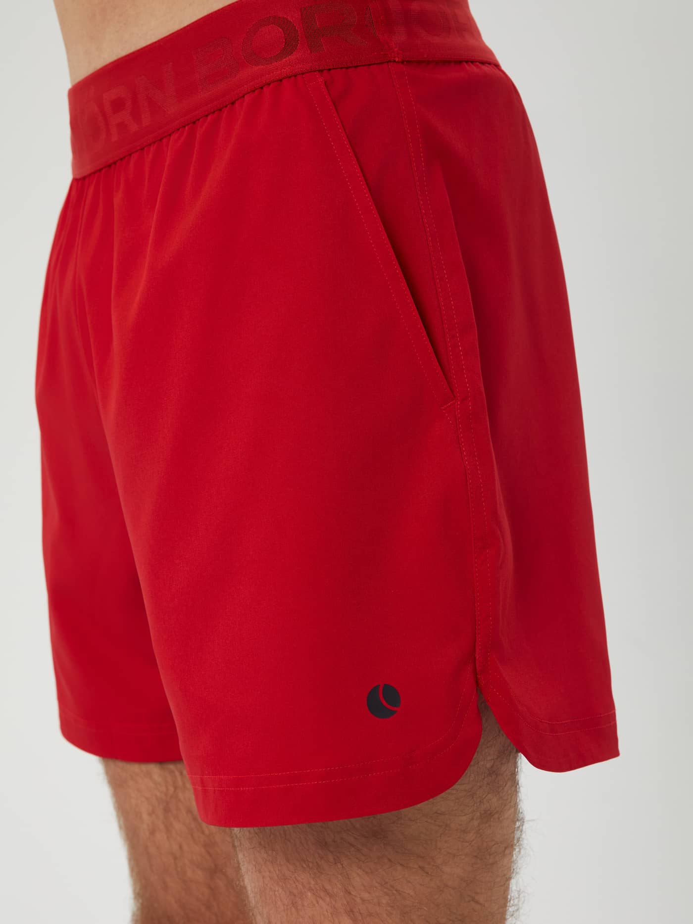 Side view of the Björn Borg Ace Short Shorts in Samba (Red) showing the side slit and tennis ball logo for training. - Image 4