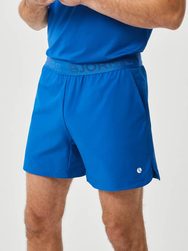 Front view of a model in Björn Borg Ace Short Shorts in Classic Blue (Blue), training shorts with a white tennis ball logo.