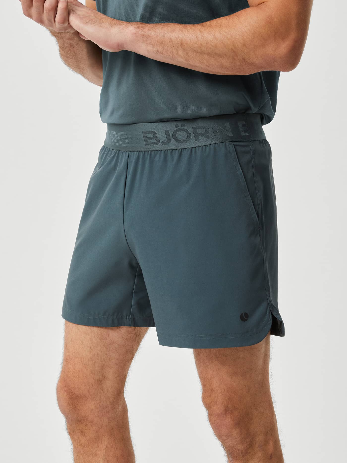 Side view of a man wearing Björn Borg Ace Short Shorts in Urban Chic (Green) with a branded waistband for tennis training. - Image 2