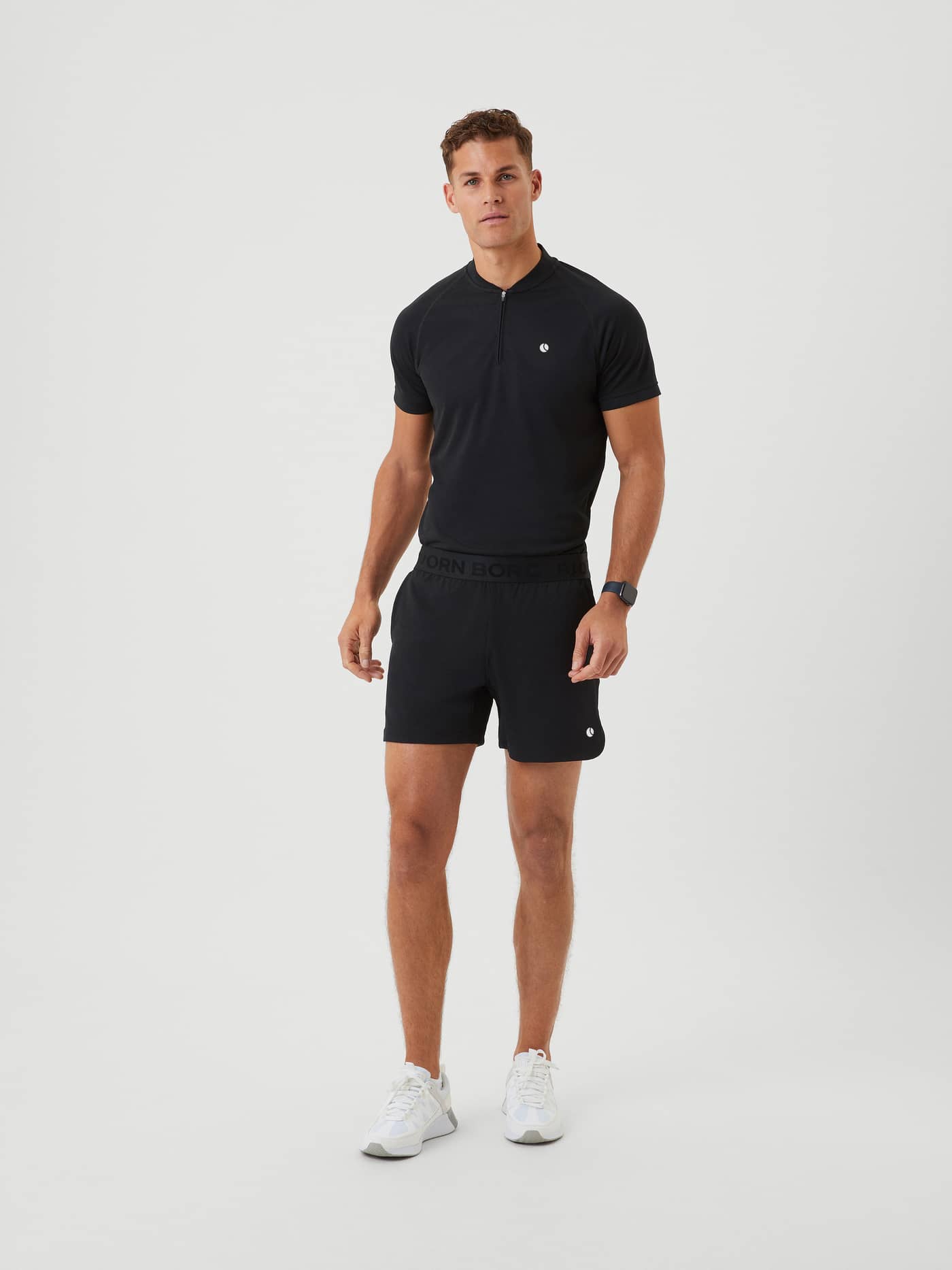 Full-body front view of a man in Björn Borg Ace Short Shorts in Black Beauty (Black) with a white logo for tennis training. - Image 1