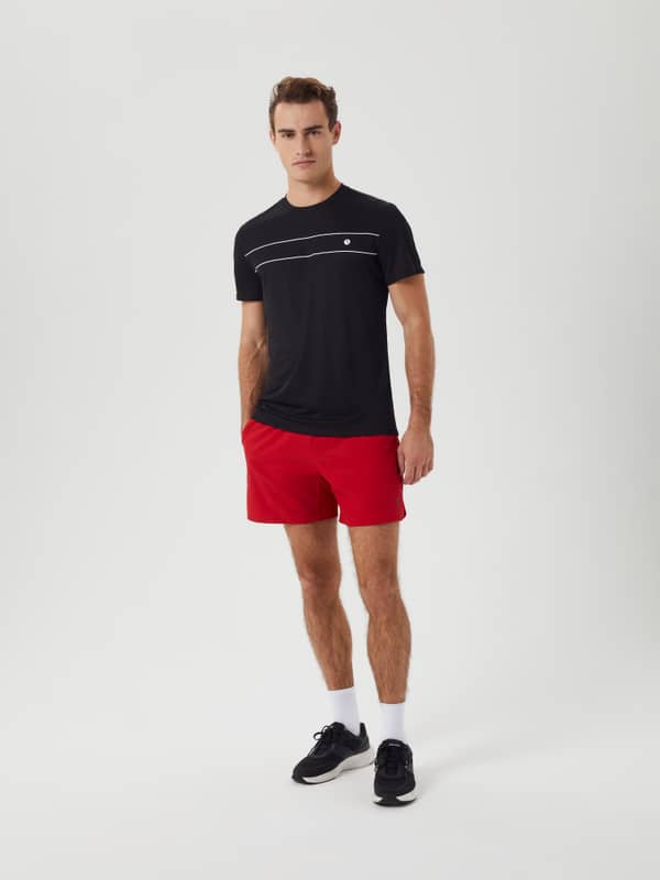Full-body front view of a model wearing the Björn Borg Ace Short Shorts in Samba (Red) for tennis training.