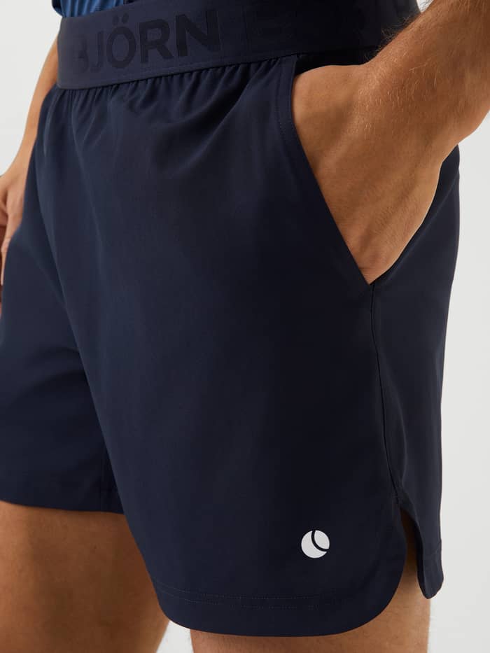 Nærbillede af Ace Short Shorts i Night Sky (Mørkeblå) med sidelomme og hvidt tennisbold-logo til tennis. - Image 4