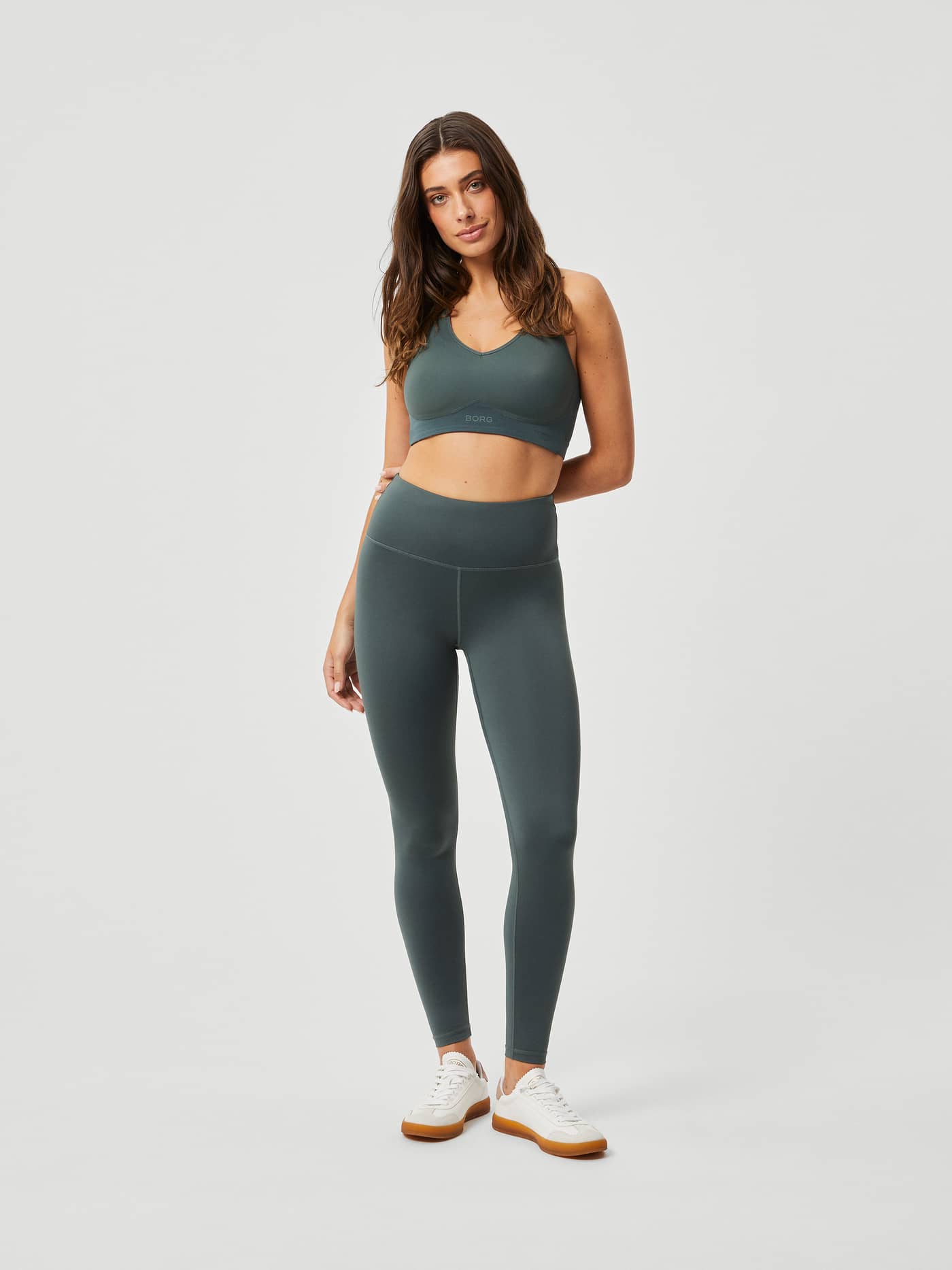 Full-body front view of a woman wearing the green Borg Mid V Support training bra and matching leggings for a stylish fit. - Image 3