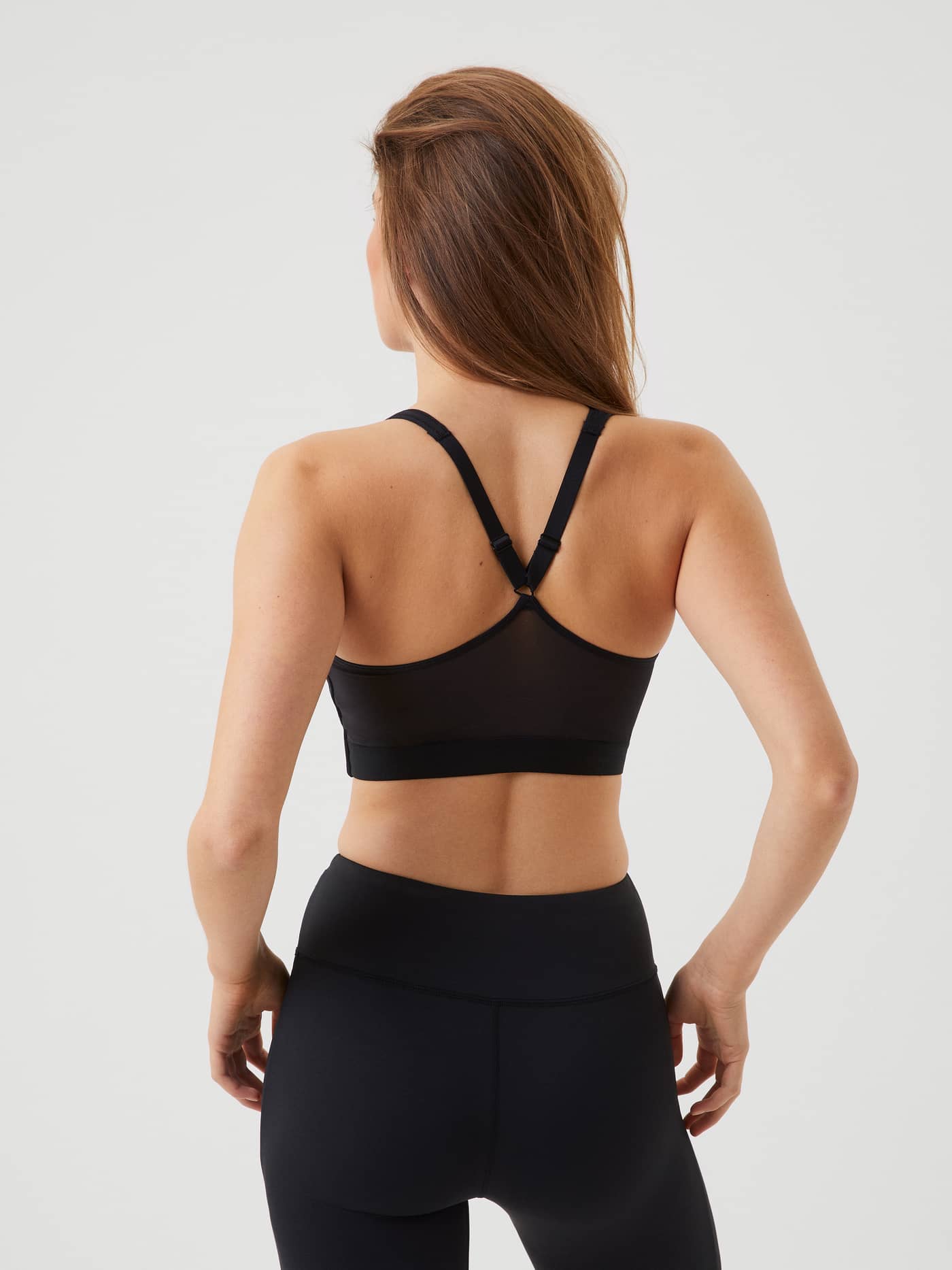 Back view of a model wearing the black Borg Mid V Support training bra featuring a mesh back and adjustable straps. - Image 2