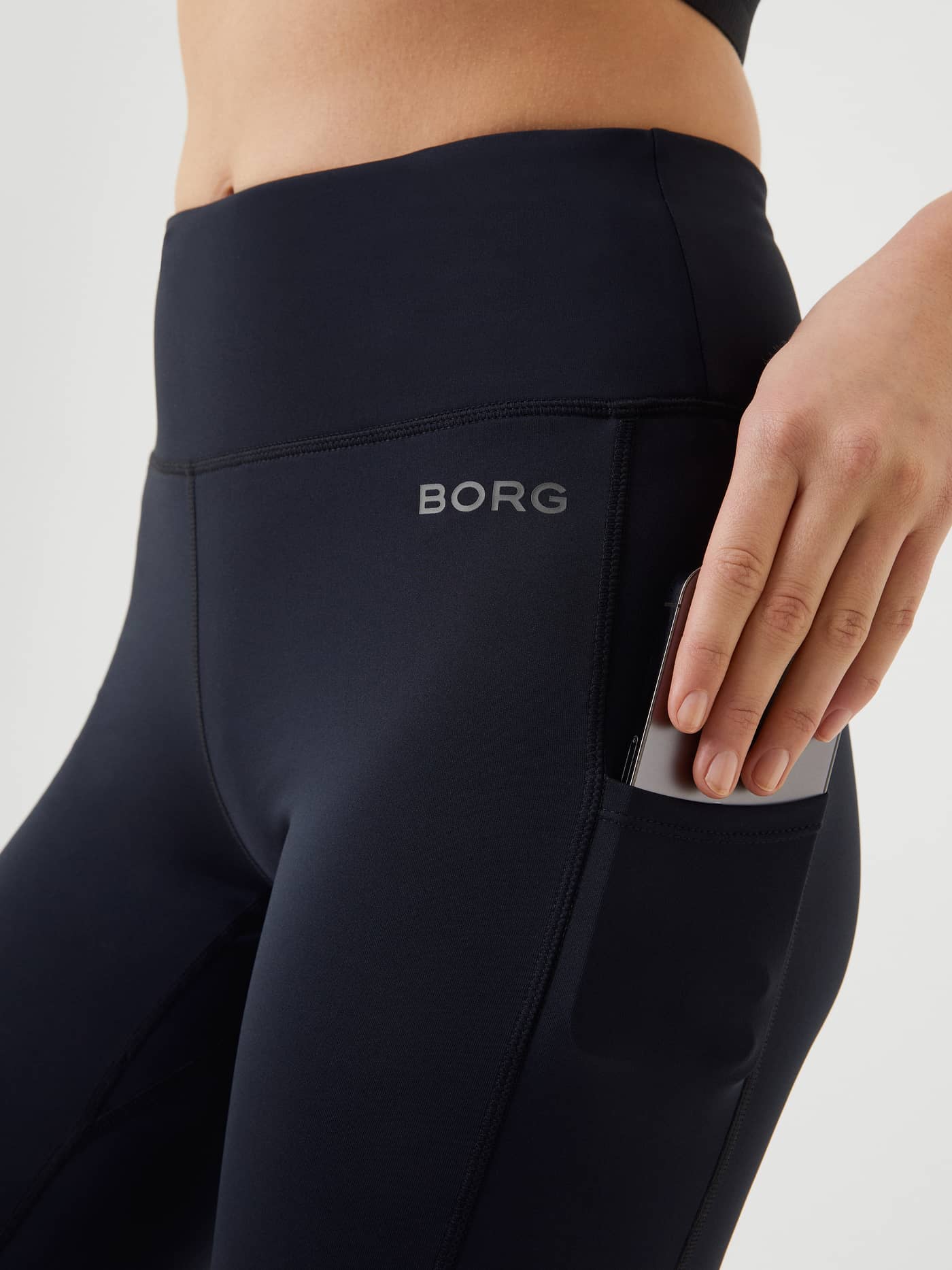 Nahaufnahme der Borg Running Winter Tights in Black Beauty (Schwarz) mit silbernem Logo und praktischer Handy-Tasche. - Image 4