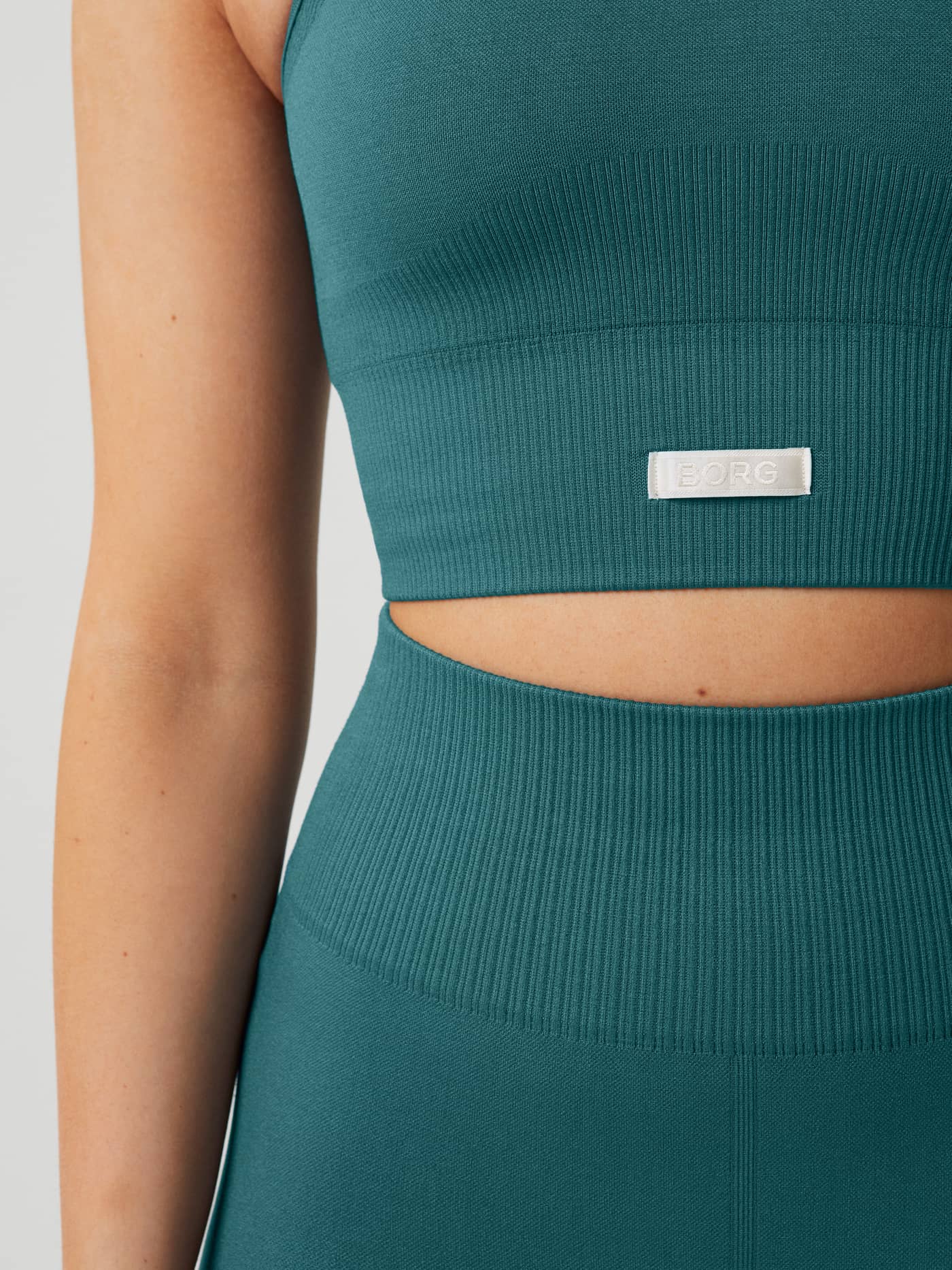 Close-up of the Studio Seamless Bralette in Mallard Blue (Blue) featuring a white BORG logo and rib-knitted training fit. - Image 5