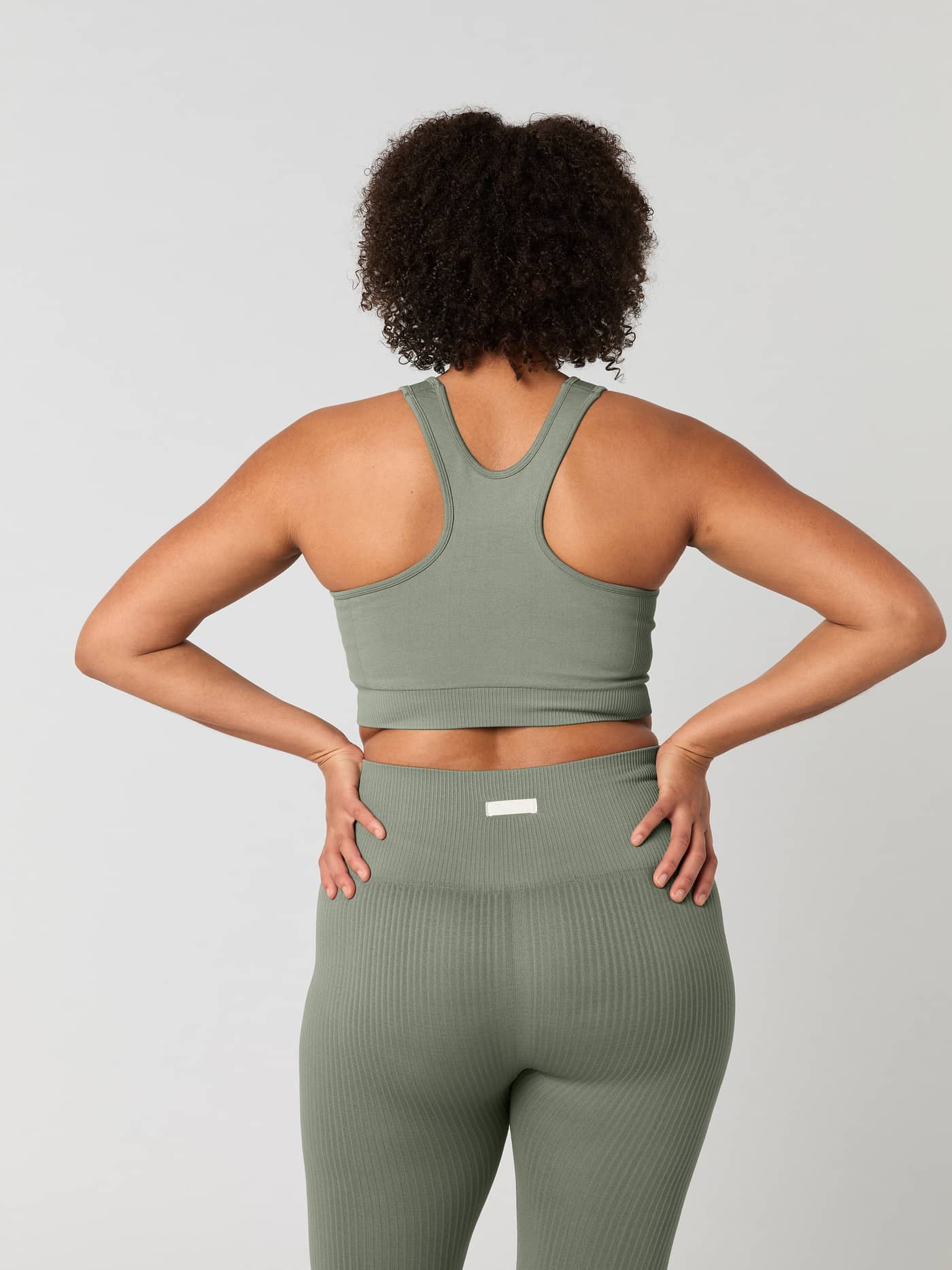 Back view of a woman wearing the green training Studio Low Seamless Bra with a seamless racerback fit. - Image 2