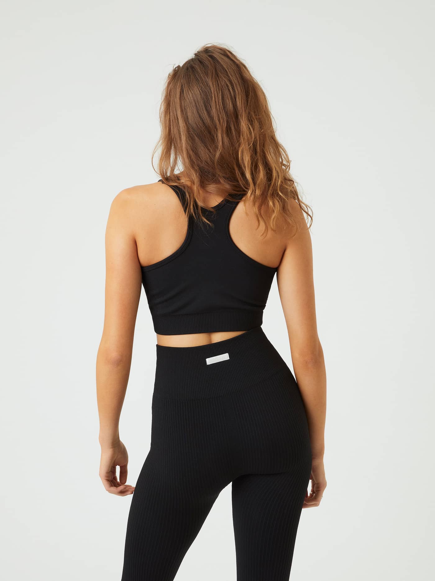 Vue de dos d'une femme portant la Studio Low Seamless Bra noire avec dos nageur offrant un bon maintien pour l'entraînement. - Image 3