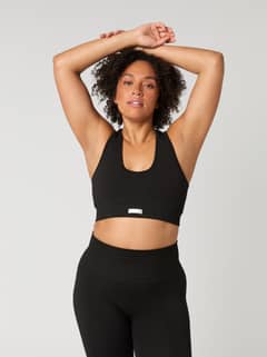 Vue de face d'une femme en Studio Low  Seamless Bra Noir, brassière d'entraînement sans coutures avec logo blanc. - Image 2