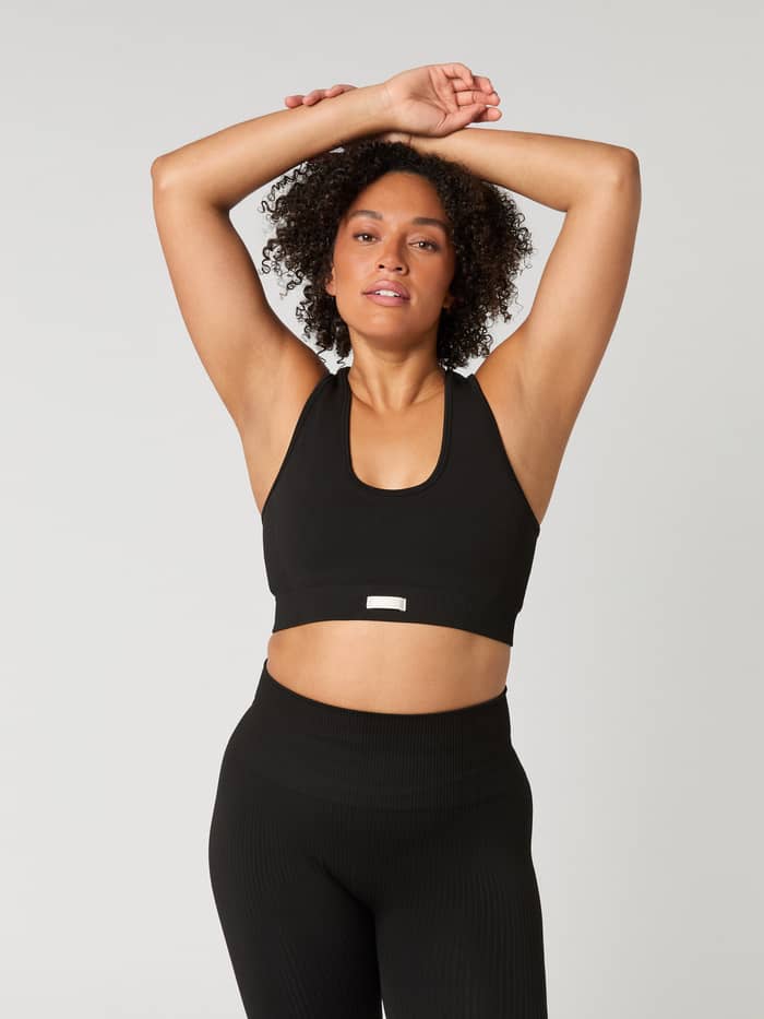 Vorderansicht einer Frau im Björn Borg Studio Low Seamless Bra in Black (Schwarz), nahtloses Trainingstop mit weißem Logo. - Image 2