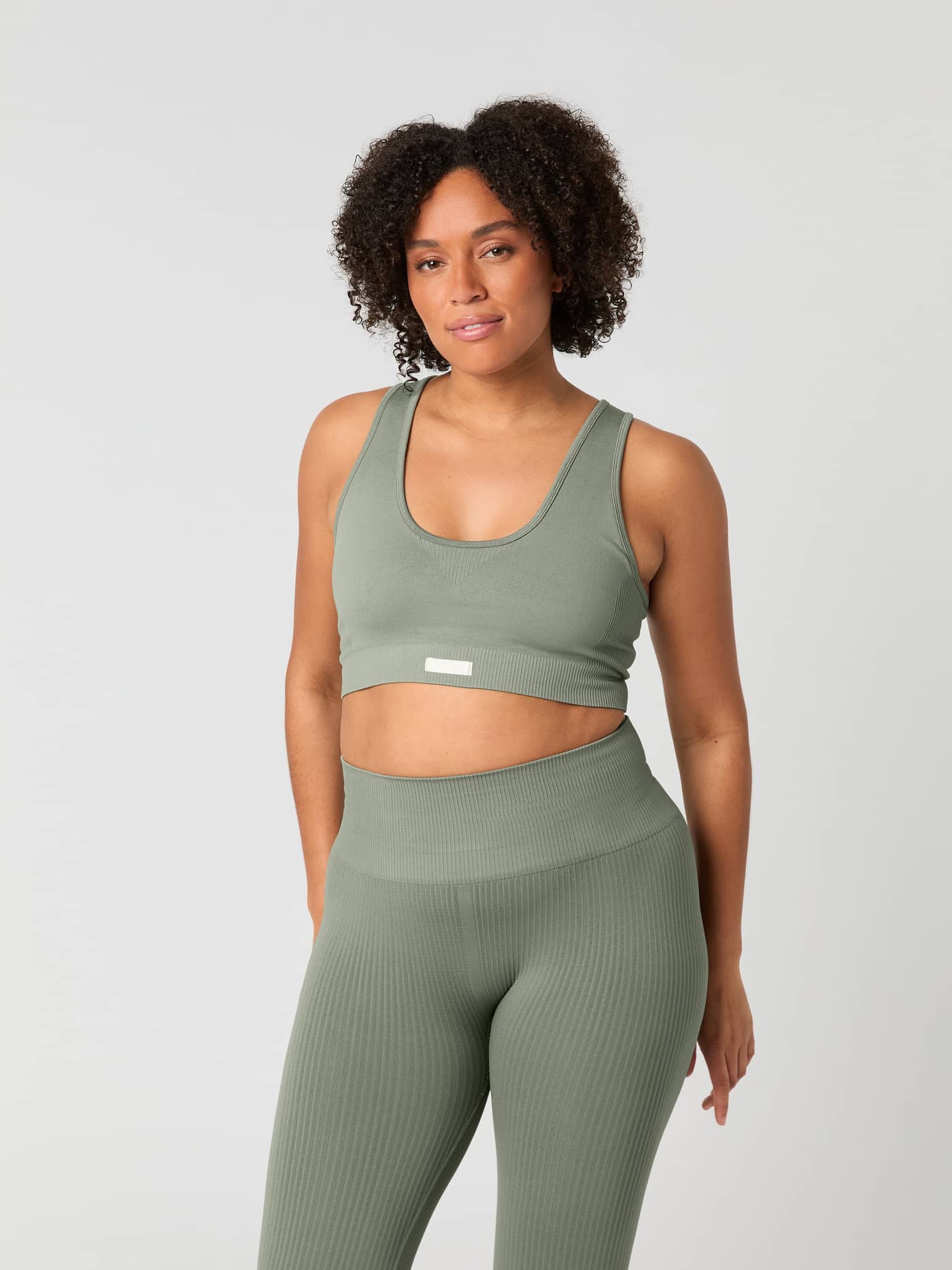 Front view of a woman wearing the Studio Low Seamless Bra in Vetiver (Green) for a comfortable seamless training fit. - Image 1