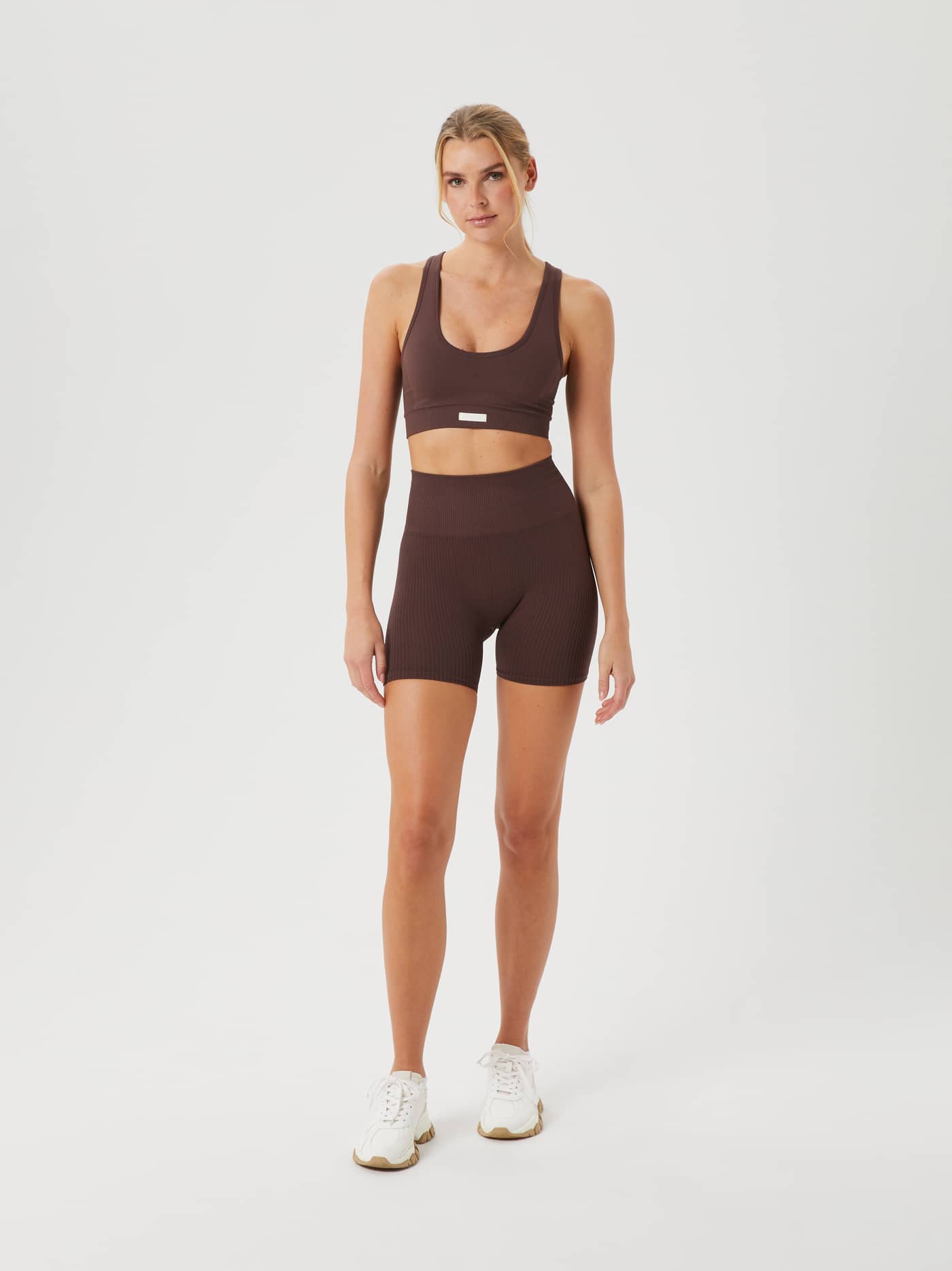 Full-body front view of a woman wearing the Björn Borg Studio Low  Seamless Bra in Brown with matching training shorts. - Image 5