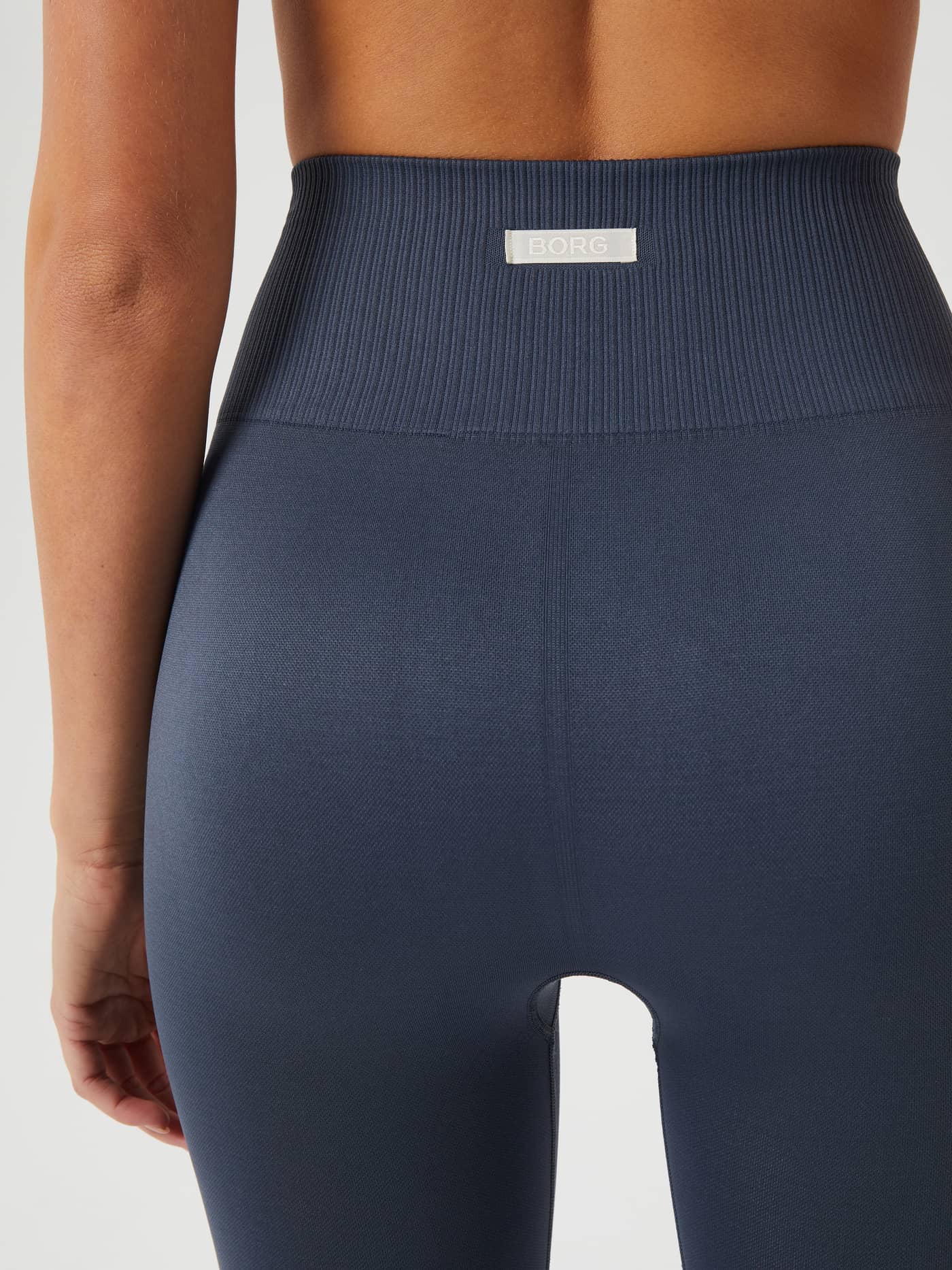 Back view of a model wearing the training Studio Seamless Light Tights in Midnight Navy (Navy) featuring a white logo label. - Image 4