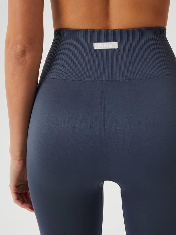 Back view of a model wearing the training Studio Seamless Light Tights in Midnight Navy (Navy) featuring a white logo label. - Image 4
