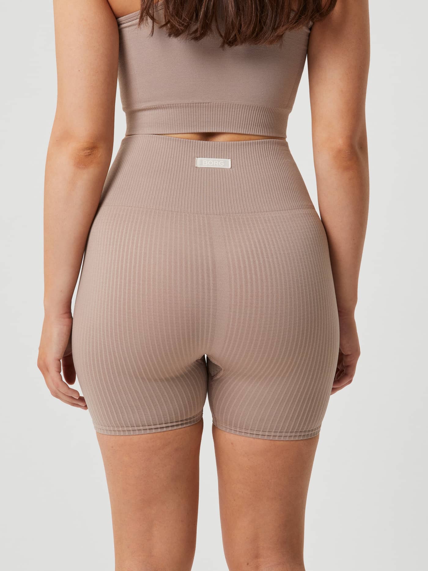 Back view of a model wearing the ribbed Studio Seamless Rib Shorts in Etherea (Beige) with a white logo for training. - Image 6