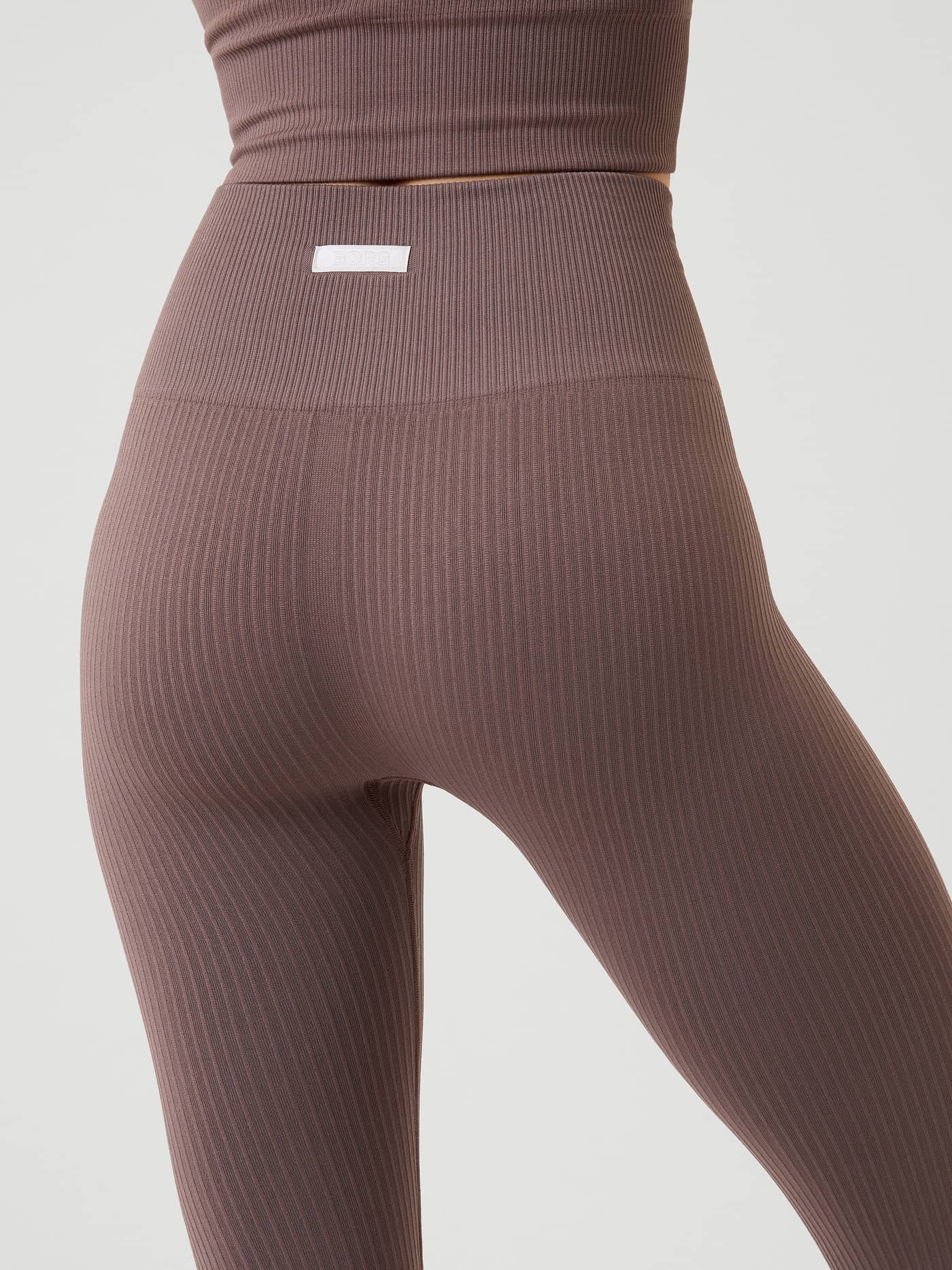 Back view of the Studio Seamless Rib Tights in Sparrow (Brown), showing the rib-knitted texture and small white logo label. - Image 4