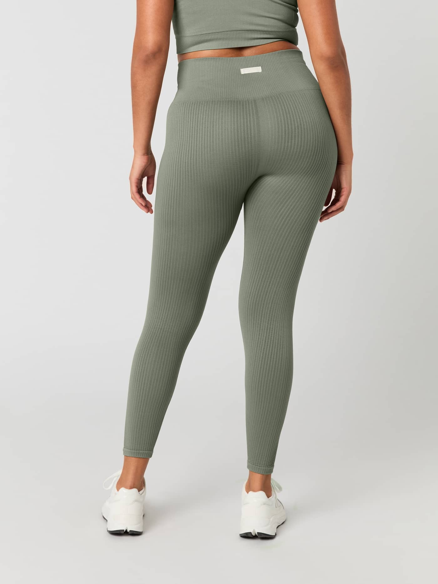 Back view of model wearing the Studio Seamless Rib Tights in Vetiver (Green) with a rib-knitted training fit and white logo. - Image 2