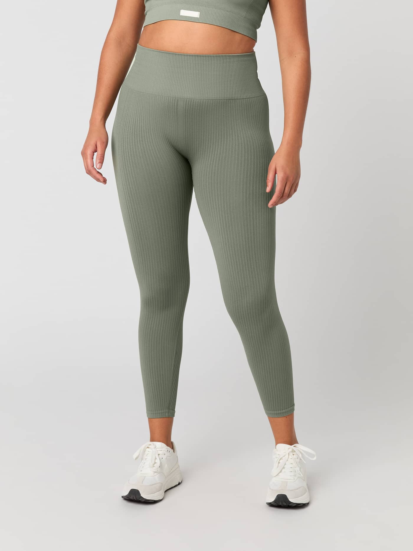 Front view of a model wearing high-waisted Studio Seamless Rib Tights in Vetiver (Green) for a supportive training fit. - Image 1