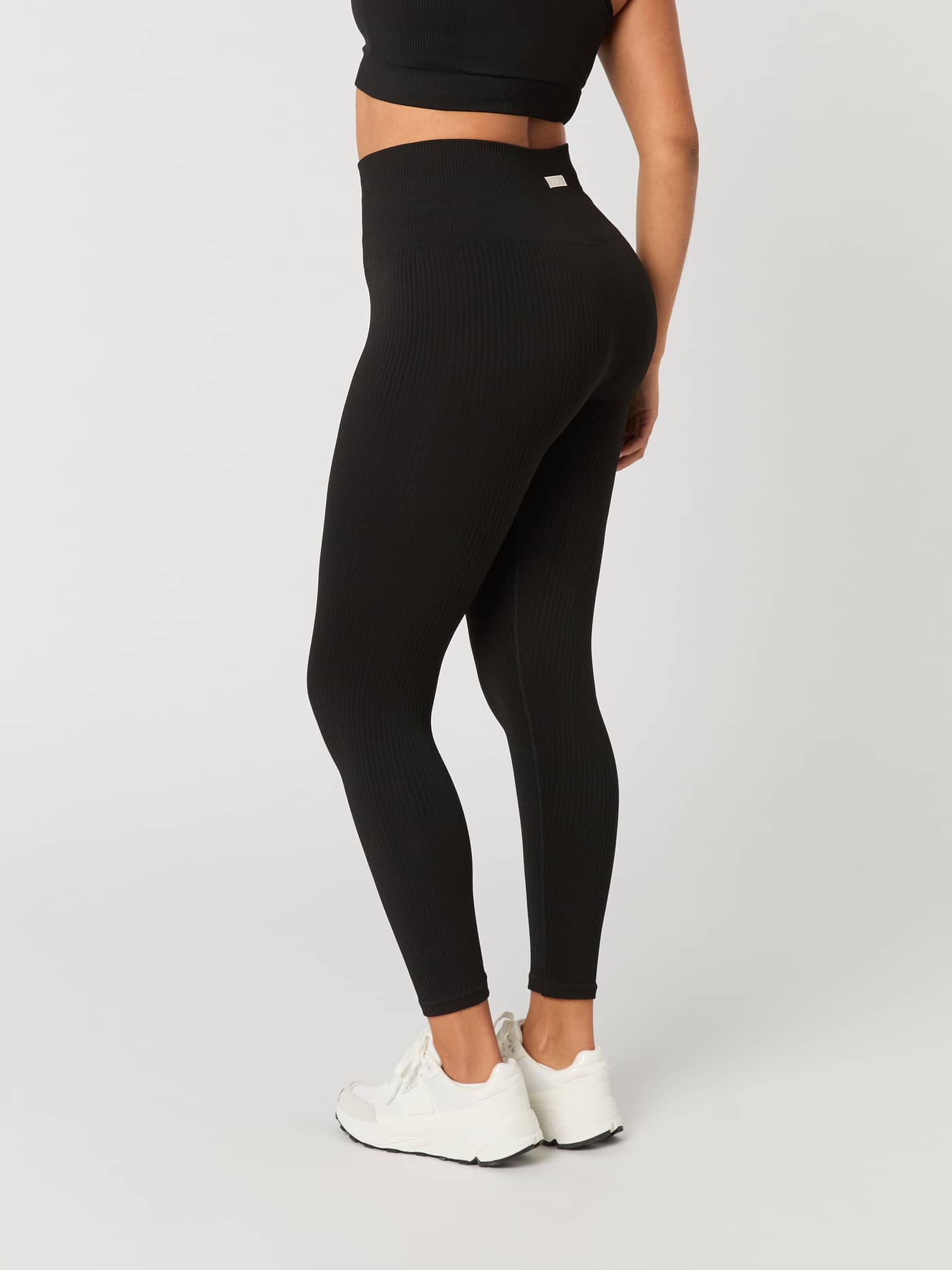 Vista lateral trasera de Studio Seamless Rib Tights en Black Beauty (Negro) de talle alto para entrenamiento con logo blanco. - Image 3