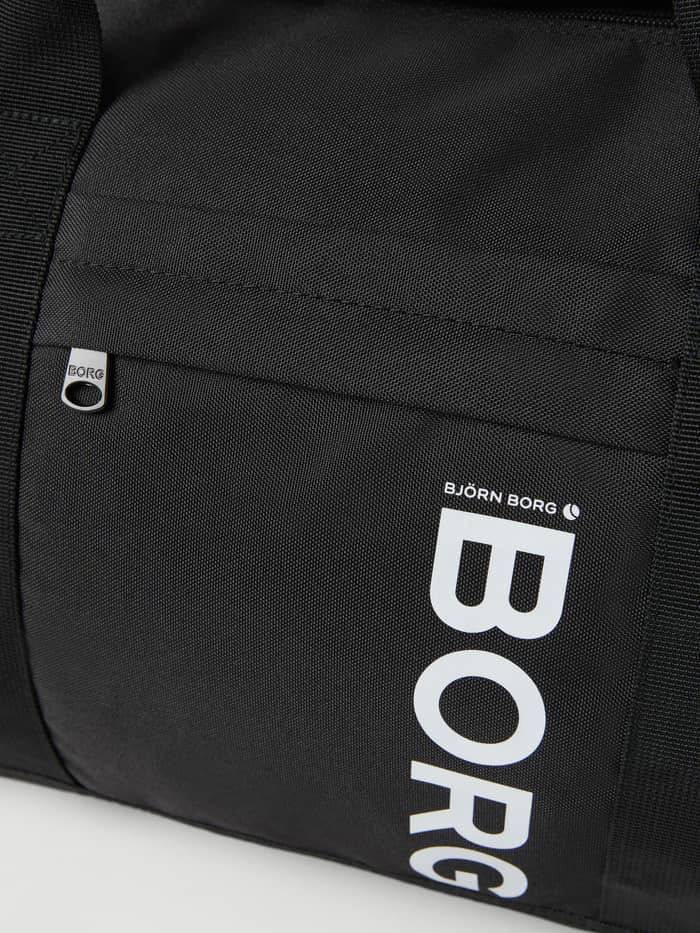 Närbild på Core Sports Bag 31L i Black Beauty (Svart) med en vit BORG-logotyp och dragkedjeficka för träning. - Image 4