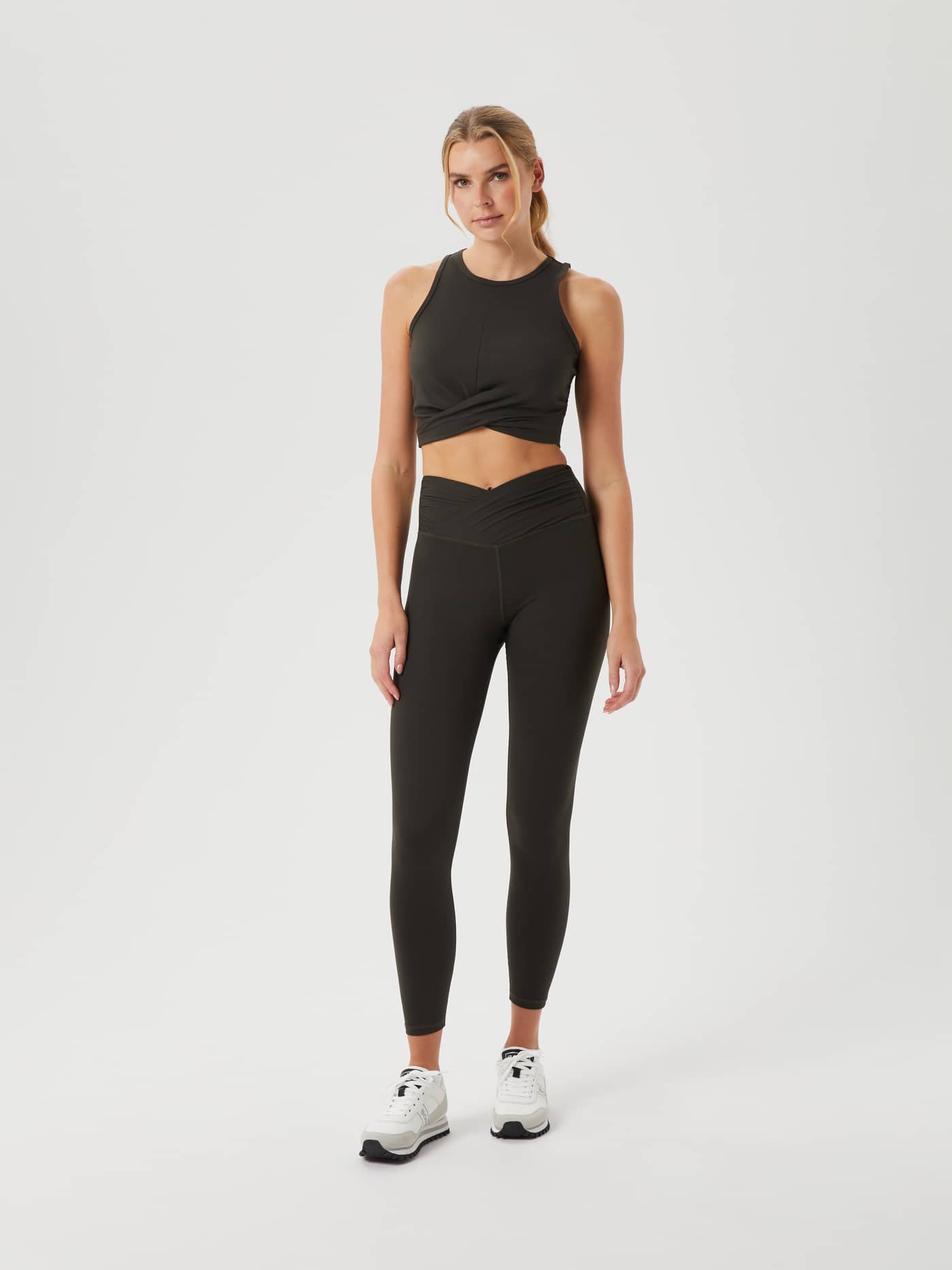 Full-body front view of a woman wearing the Björn Borg Studio Cross Tank in Peat (Green) with a twisted front for training. - Image 3