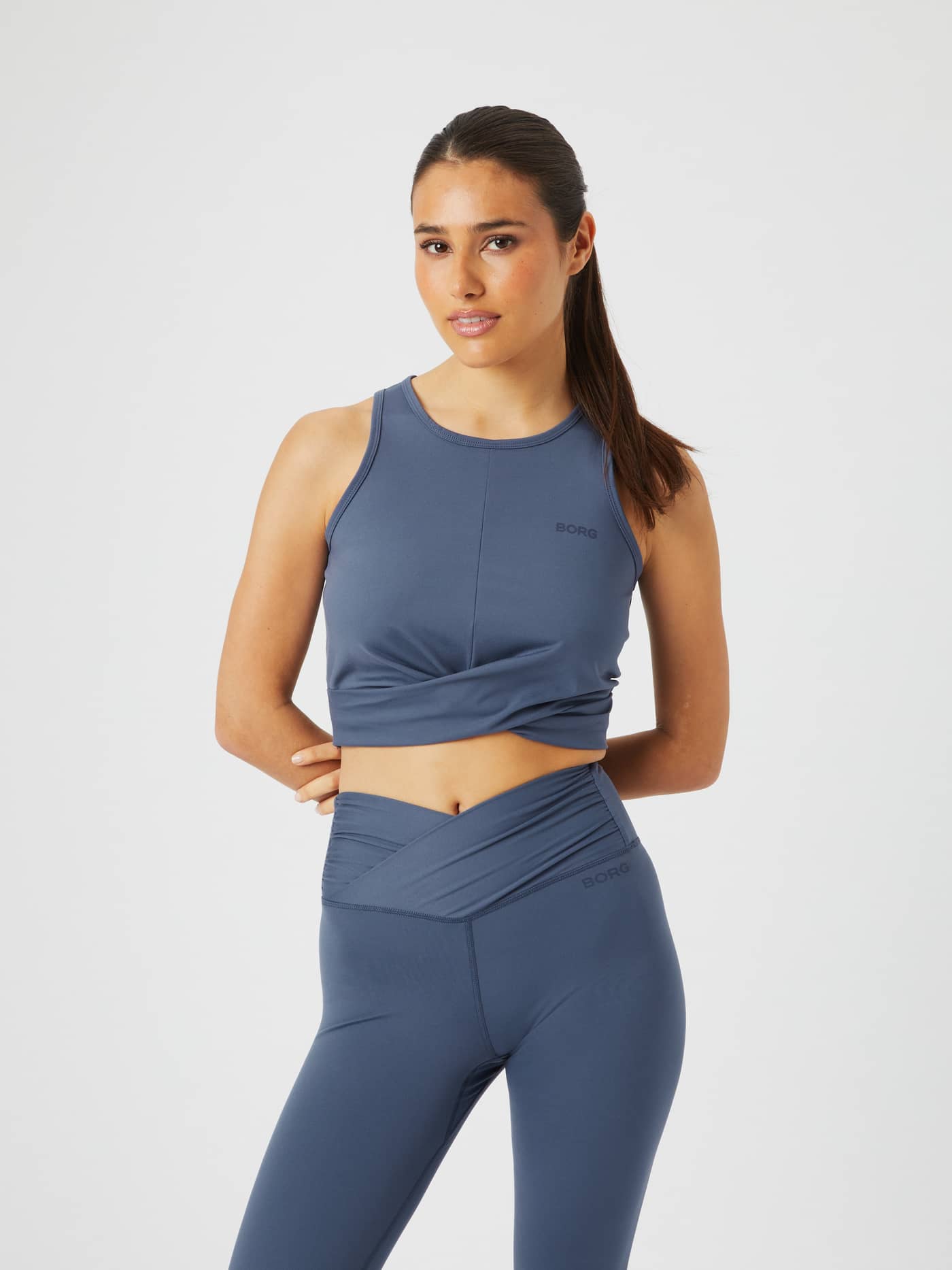 Woman wearing Studio Cross Tank in Nightshadow Blue (Blue) for training, with a stylish fit, twisted front, and dark logo. - Image 1