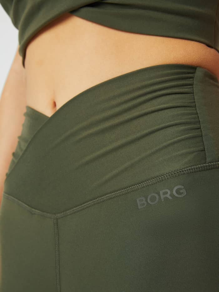 Close-up of the twisted high waist and tonal BORG logo on the Studio Cross Tights in Olive Night (Green) for training. - Image 4