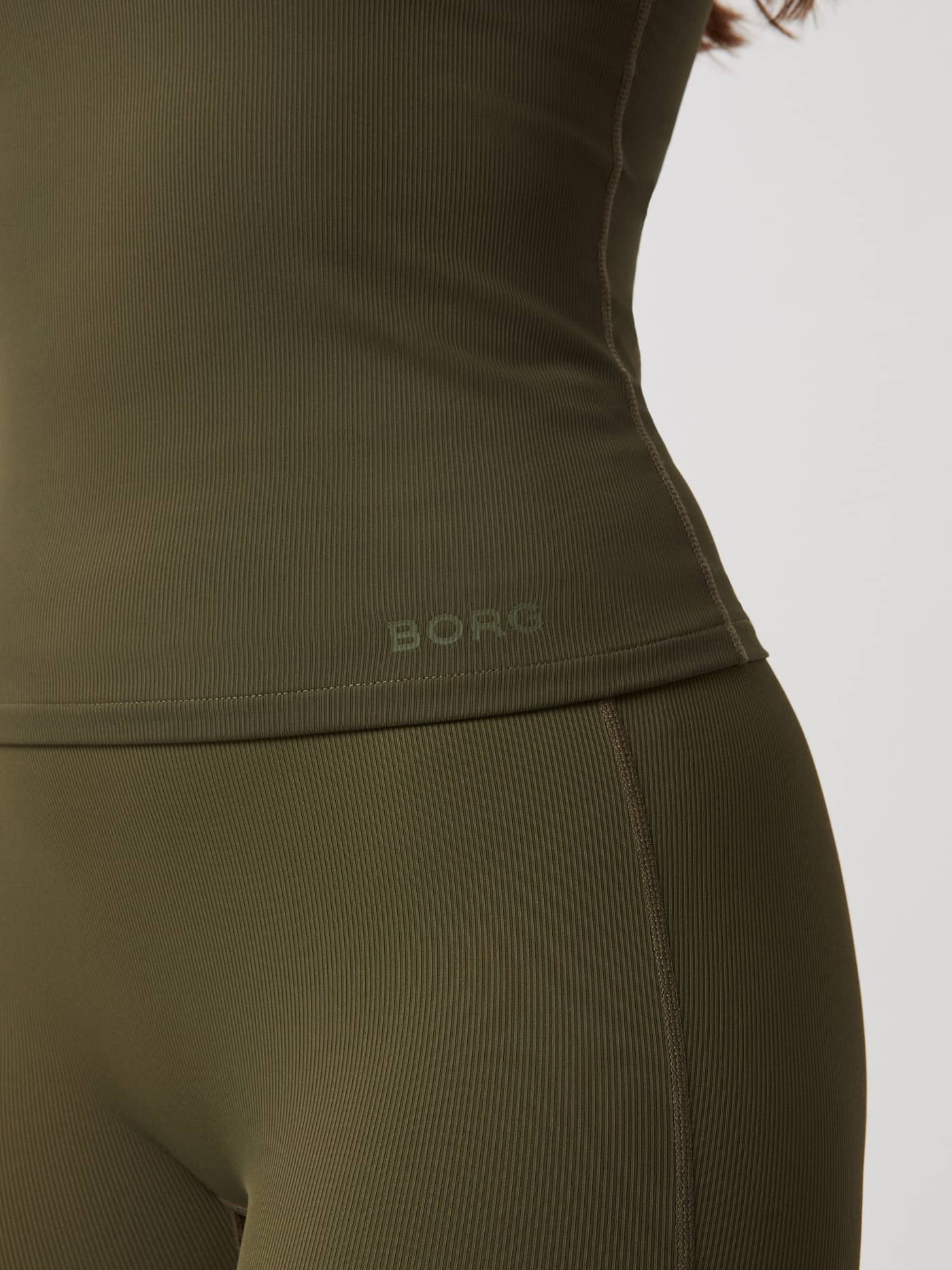 Studio Rib Strap Tank i Olive Night (grønn) med ribbestrikket treningsmateriale og grønn Borg-logo, vist i et nærbilde. - Image 5
