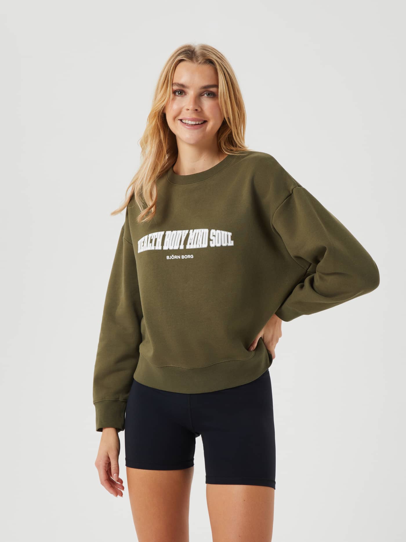 Front view of a woman wearing the oversized Björn Borg Ace Boyfriend Crew in Olive Night (Green) with a white graphic print. - Image 5