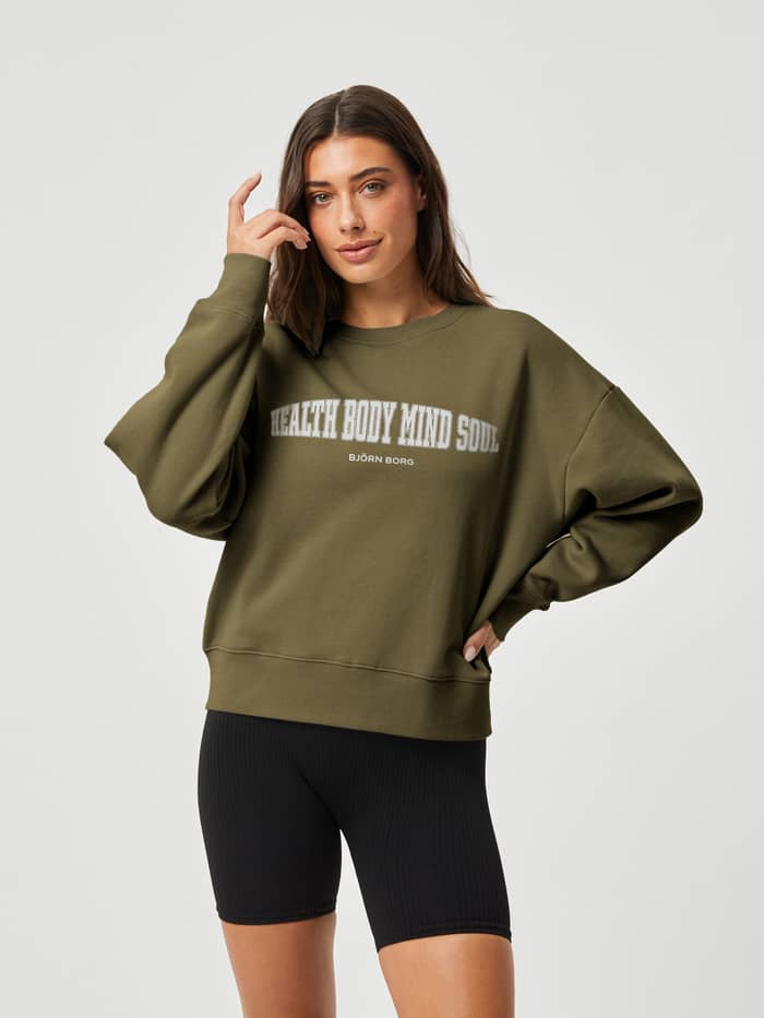Vorderansicht einer Frau im oversized Ace Boyfriend Crew aus Fleece in Ivy Green (Grün) mit weißer Brustgrafik. - Image 2