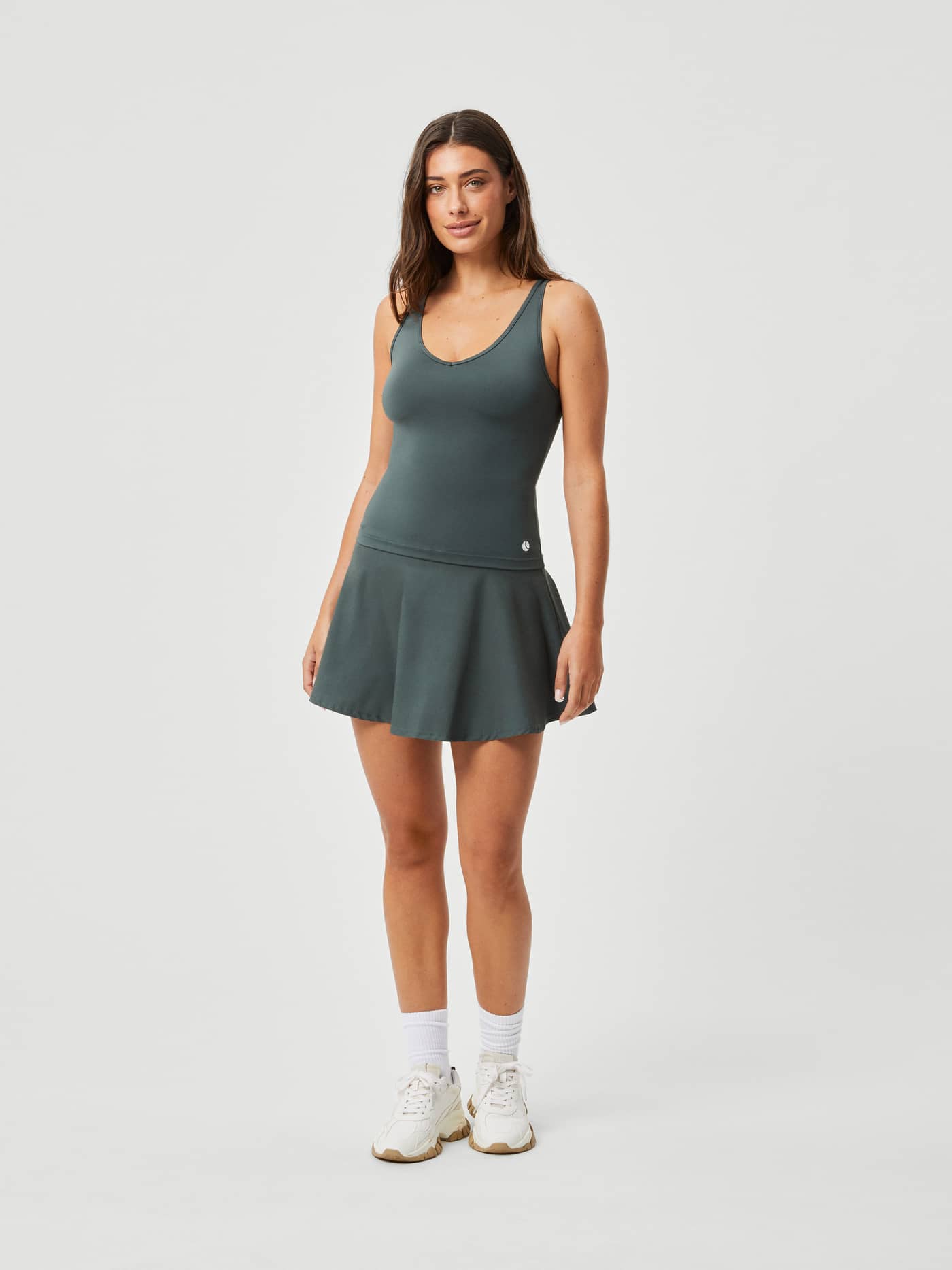 Full-body front view of a woman wearing the slim-fit Ace Deep V Tank in Urban Chic (Green), perfect for tennis or training. - Image 3