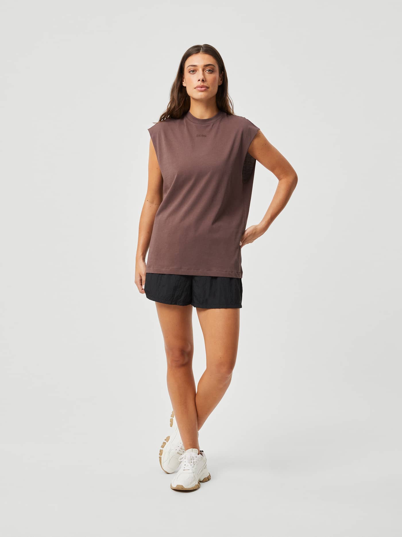 Full-body front view of a woman wearing the Studio Loose Fit Tank in French Toast (Brown) with a tonal logo for training. - Image 3