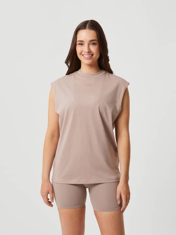 Vista frontal de una modelo con la Studio Loose Fit Tank en Etherea (Beige), top de entrenamiento holgado con logo a tono.