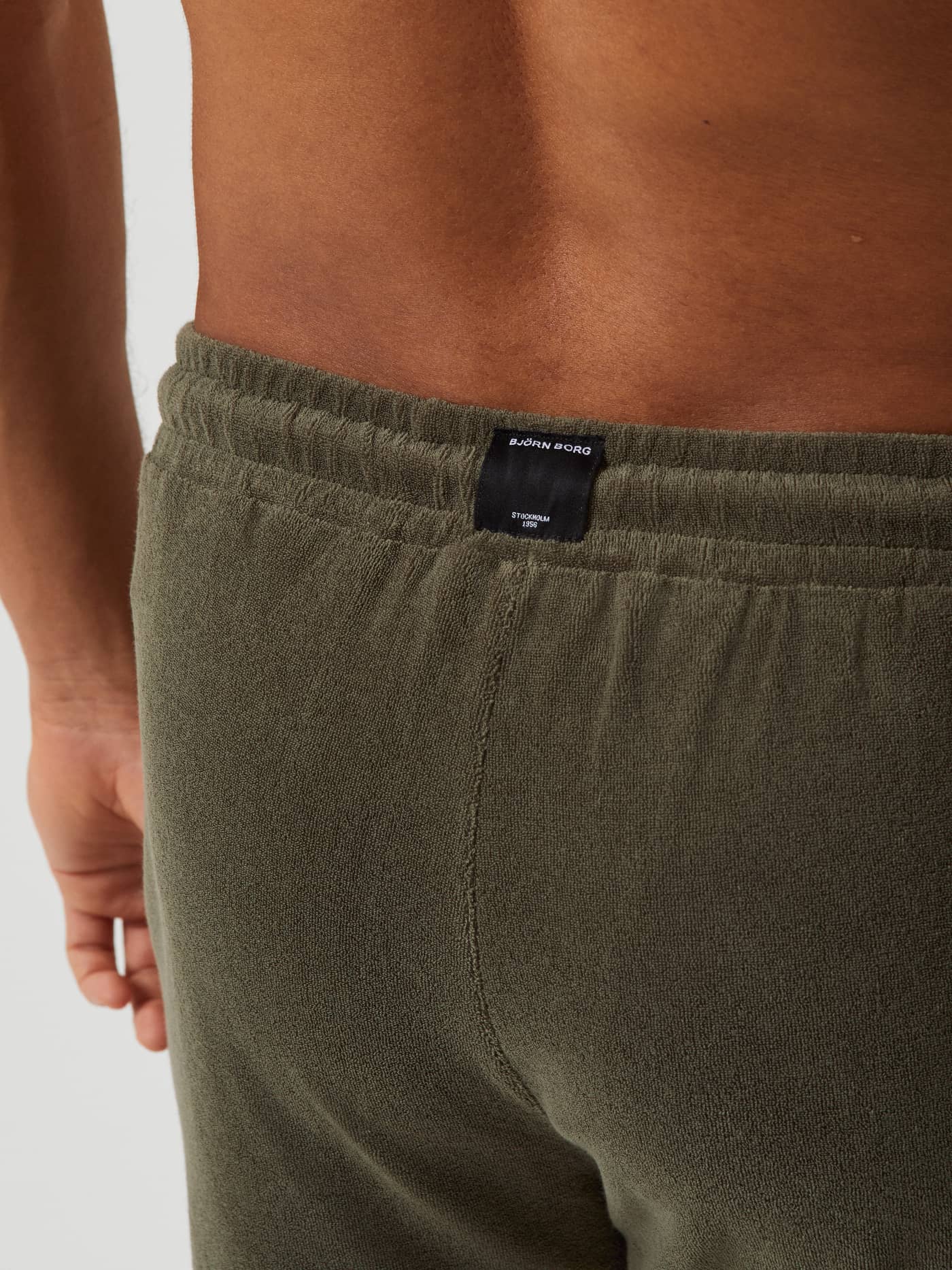 Närbild bakifrån på Borg Toweling Pool Shorts i Beetle (Grön) i mjuk frotté med en svart vävd logotypetikett. - Image 4