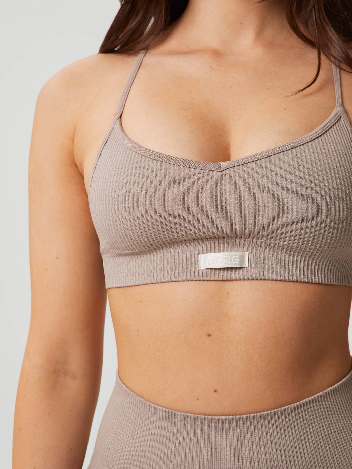 Close-up of the Studio Seamless Ribbed Strap Bra in Etherea (Beige), featuring a white woven logo and a stylish fit. - Image 3