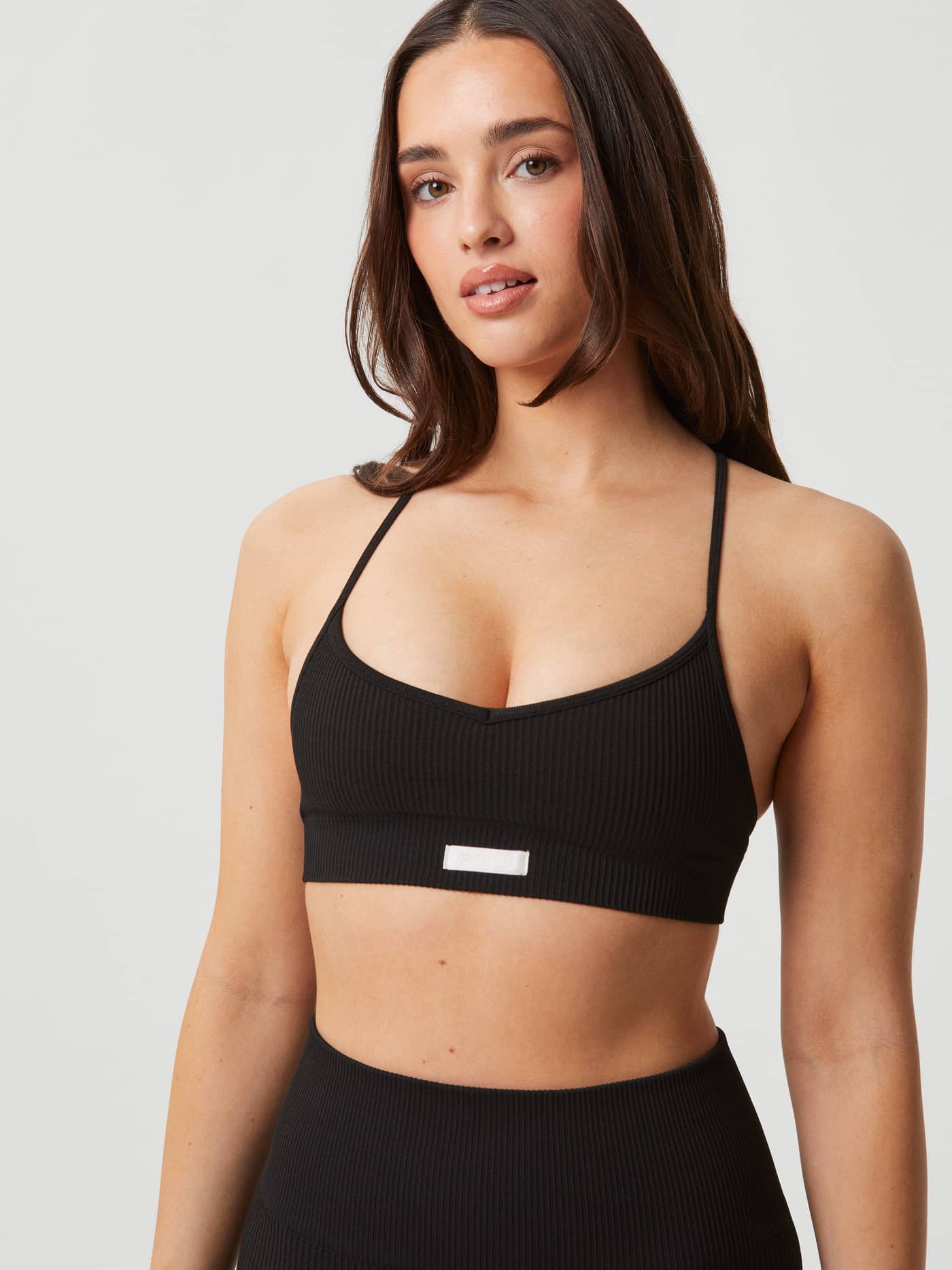 Studio Seamless Ribbed Strap Bra in zwart met een wit logolabel en een stijlvolle, naadloze pasvorm in vooraanzicht. - Image 5