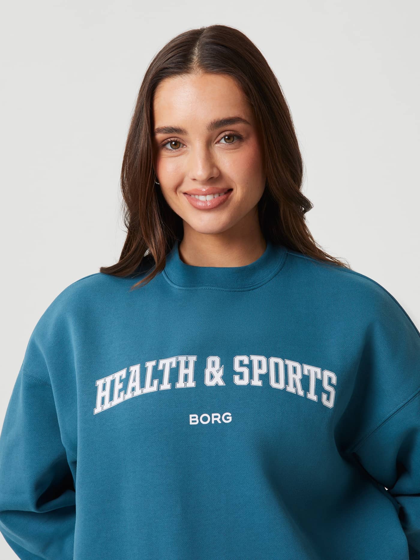 Front close-up of a model in the Mallard Blue (Blue) Studio Oversized Crew in soft cotton with a white chest logo. - Image 5