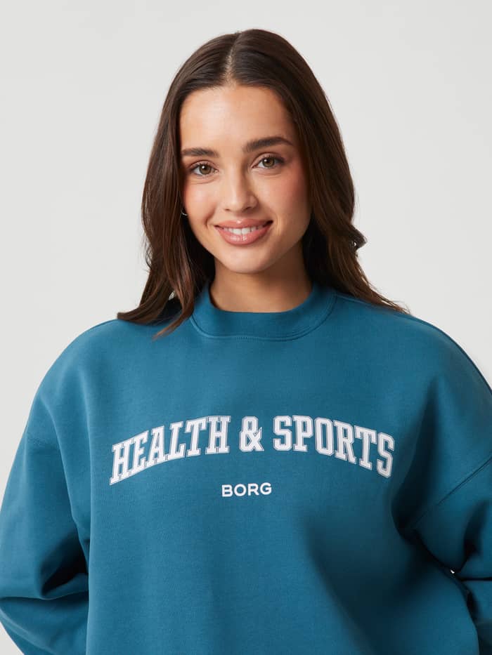 Vorderansicht eines Models im Studio Oversized Crew in Mallard Blue (Blau) aus weicher Baumwolle mit weißem Brustlogo. - Image 5