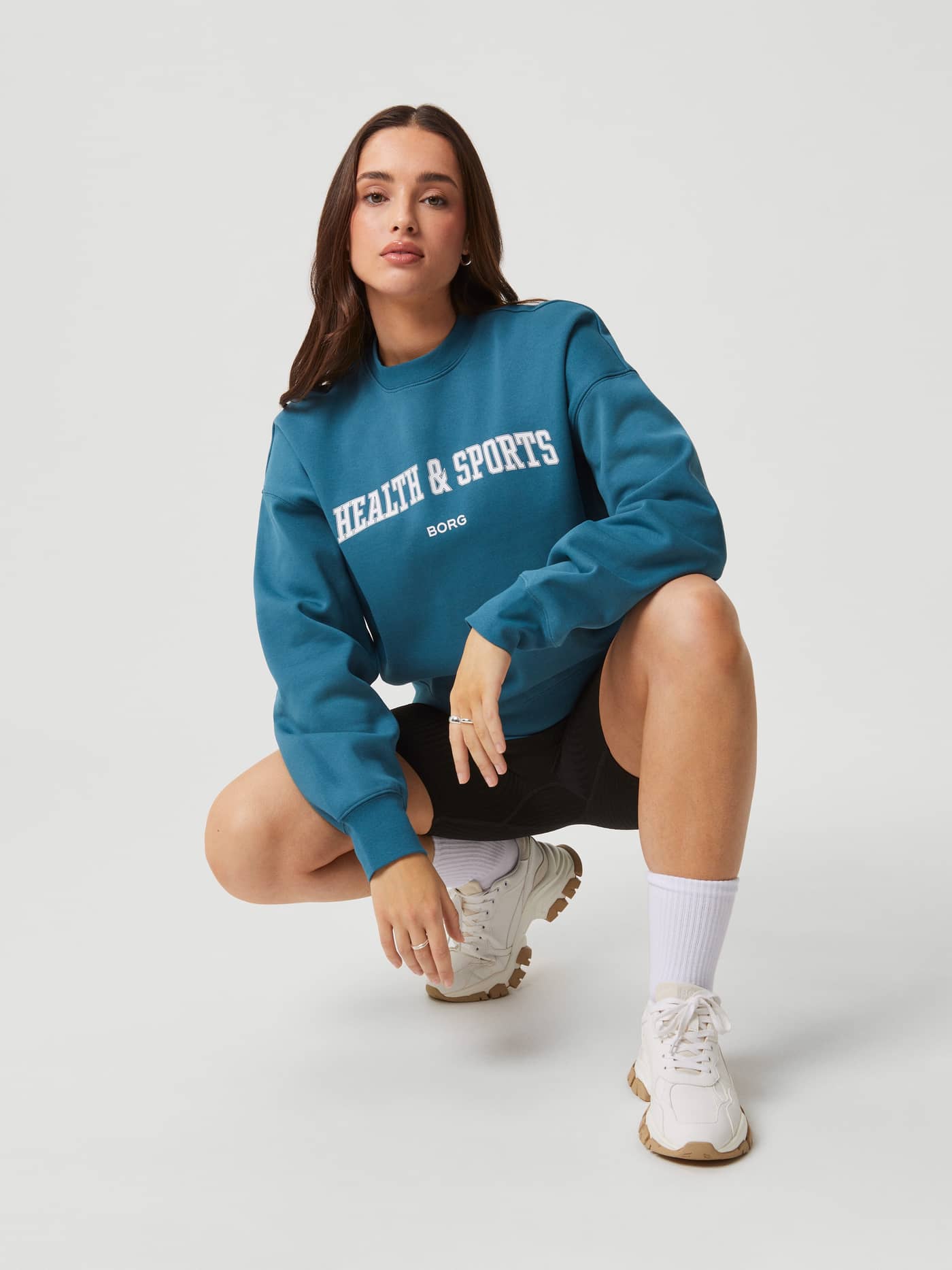 Front view of a woman in the Mallard Blue (Blue) Studio Oversized Crew in soft cotton with a white logo and oversized fit. - Image 6