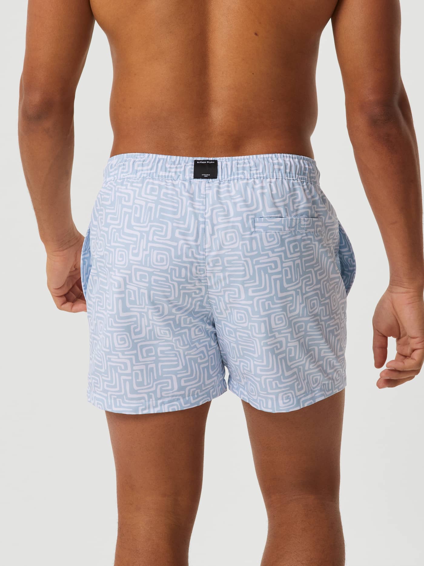 Back view of a man wearing the Borg Print Swim Shorts in Funky Big 1 (Blue) with a geometric pattern and back pocket. - Image 3
