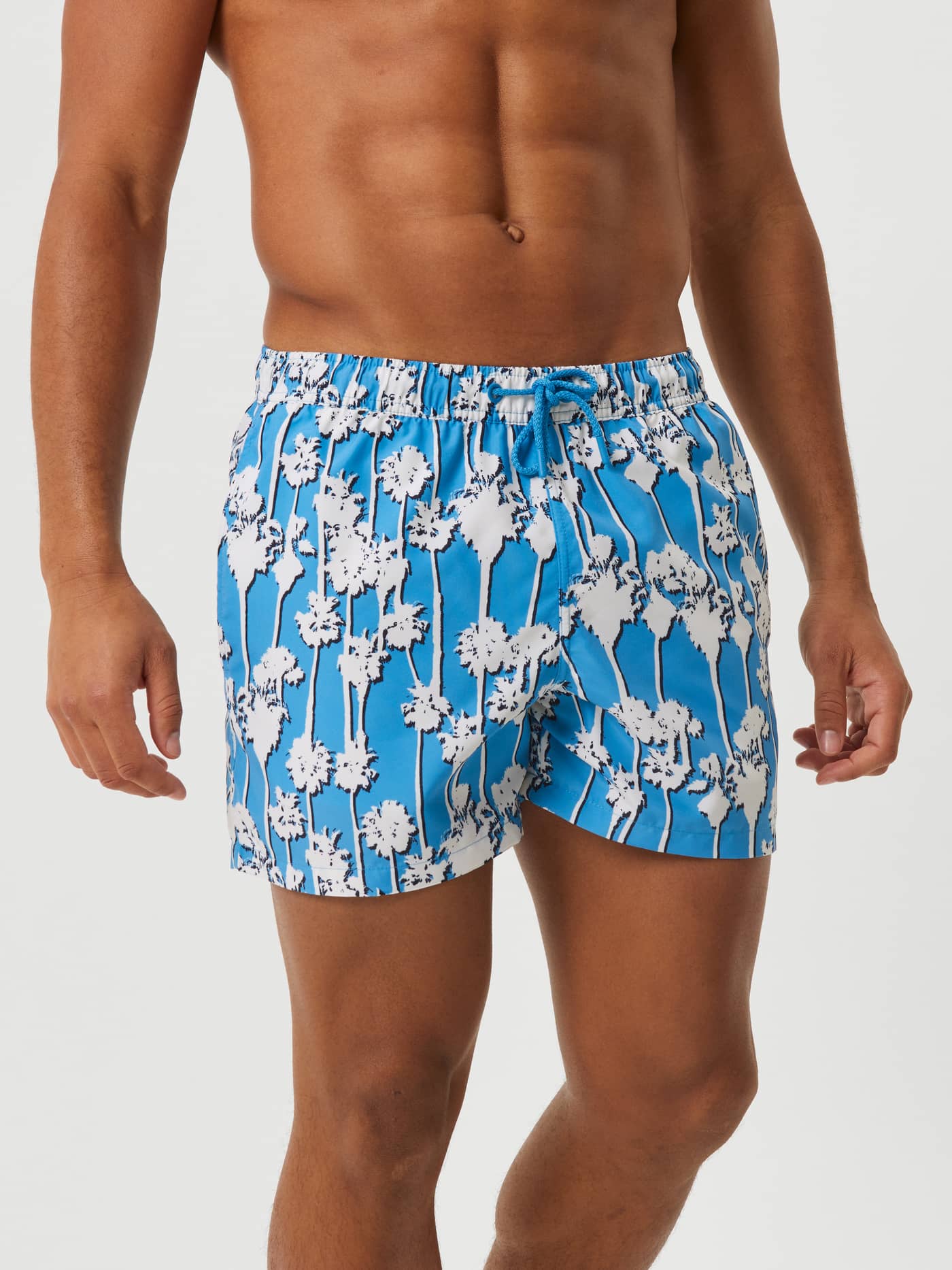 Front view of a man wearing the quick-drying Borg Print Swim Shorts in Palm Springs Big 1 (blue) with a palm tree print. - Image 2