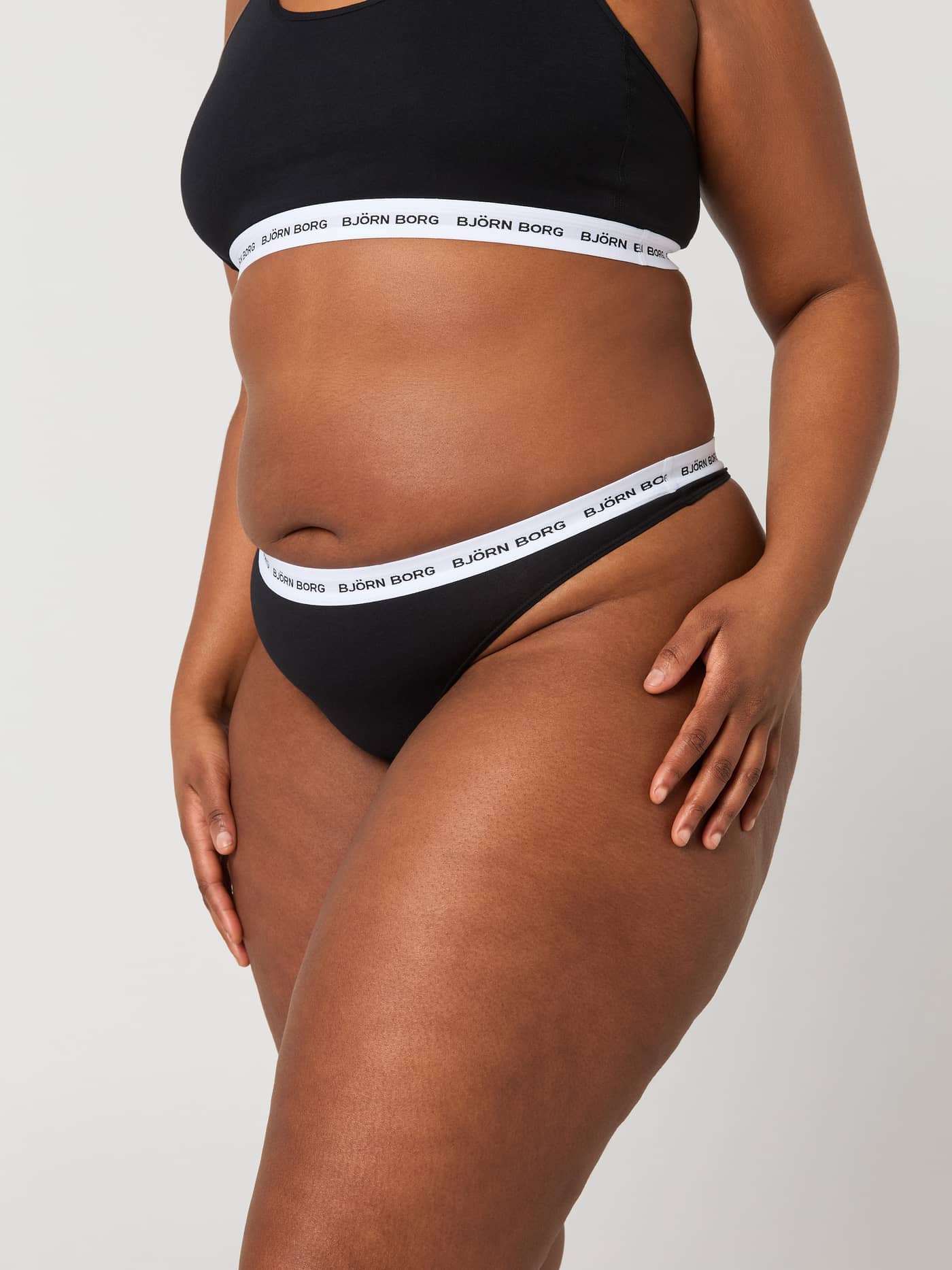 Side view of a model wearing the black Björn Borg Core Logo Thong 2-pack with a white logo elastic waistband. - Image 6